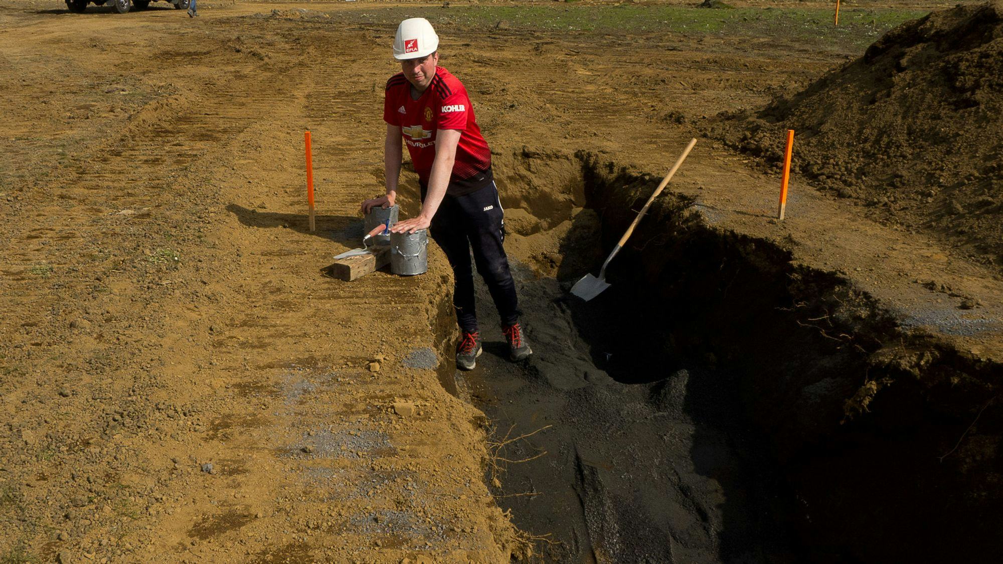 A man in a dug ground next to a shovel
