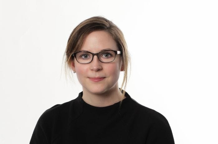 Picture of Natalie a woman with brown hair and black glasses wearing black sweater and white background