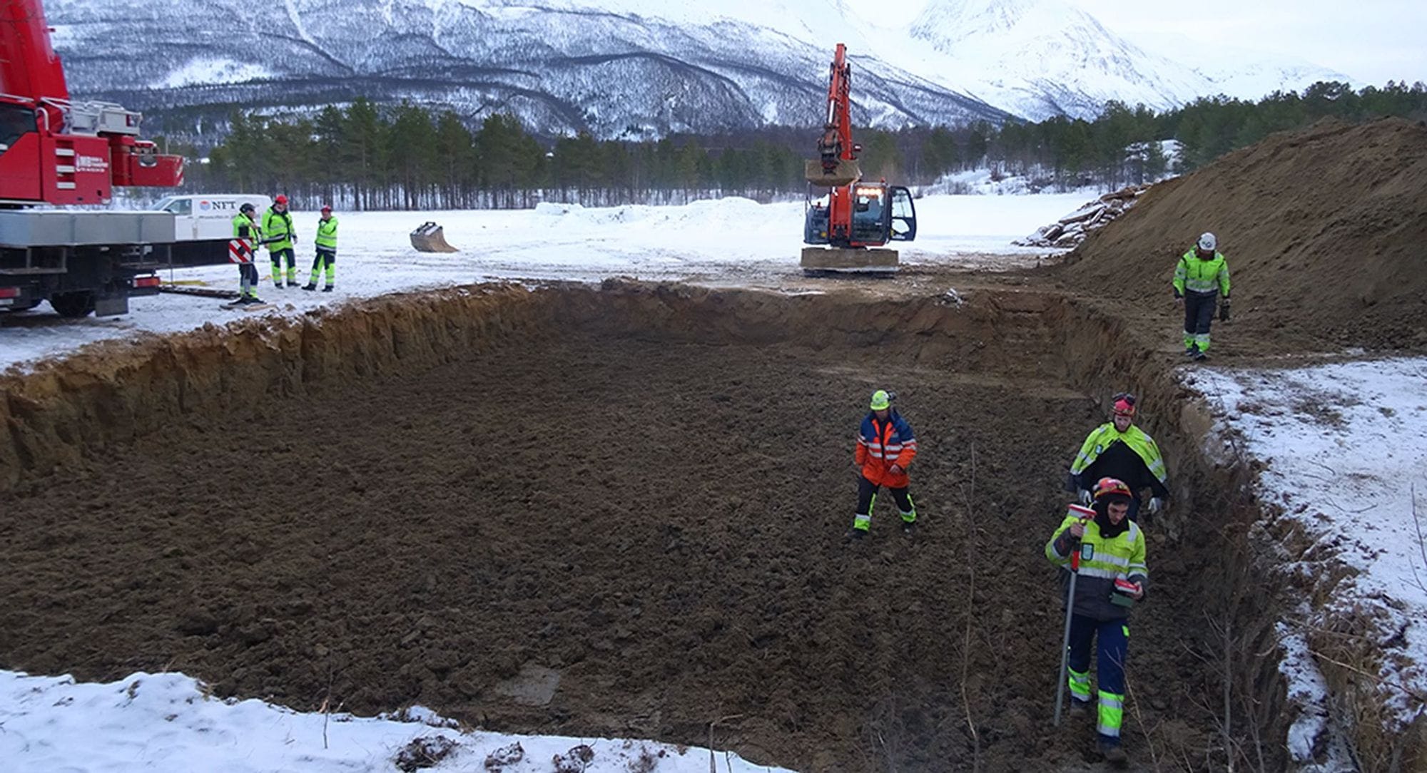 Men in safety gear digging a big hole, industrial machinery