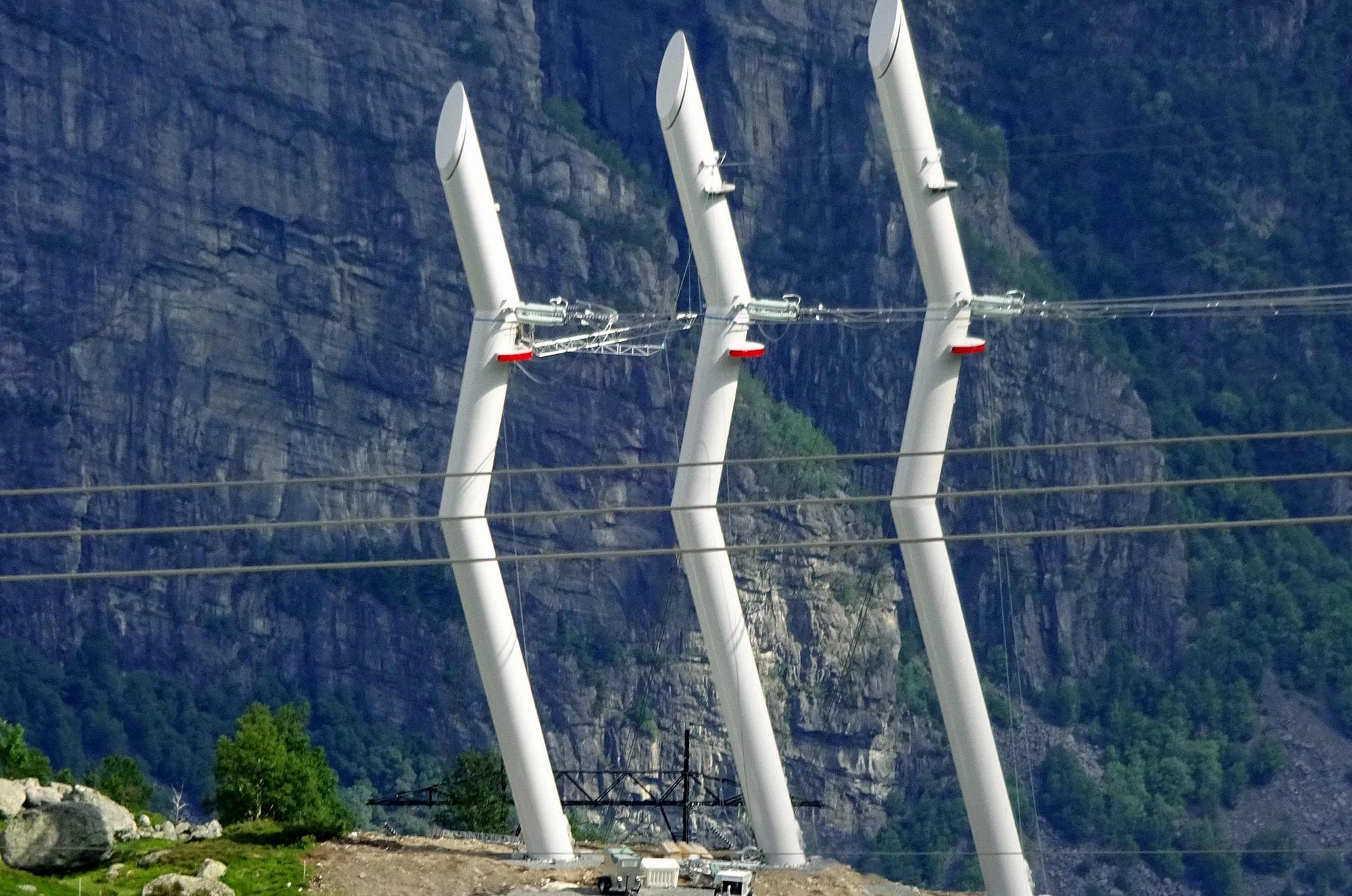 Three white design masts in front of a mountainside