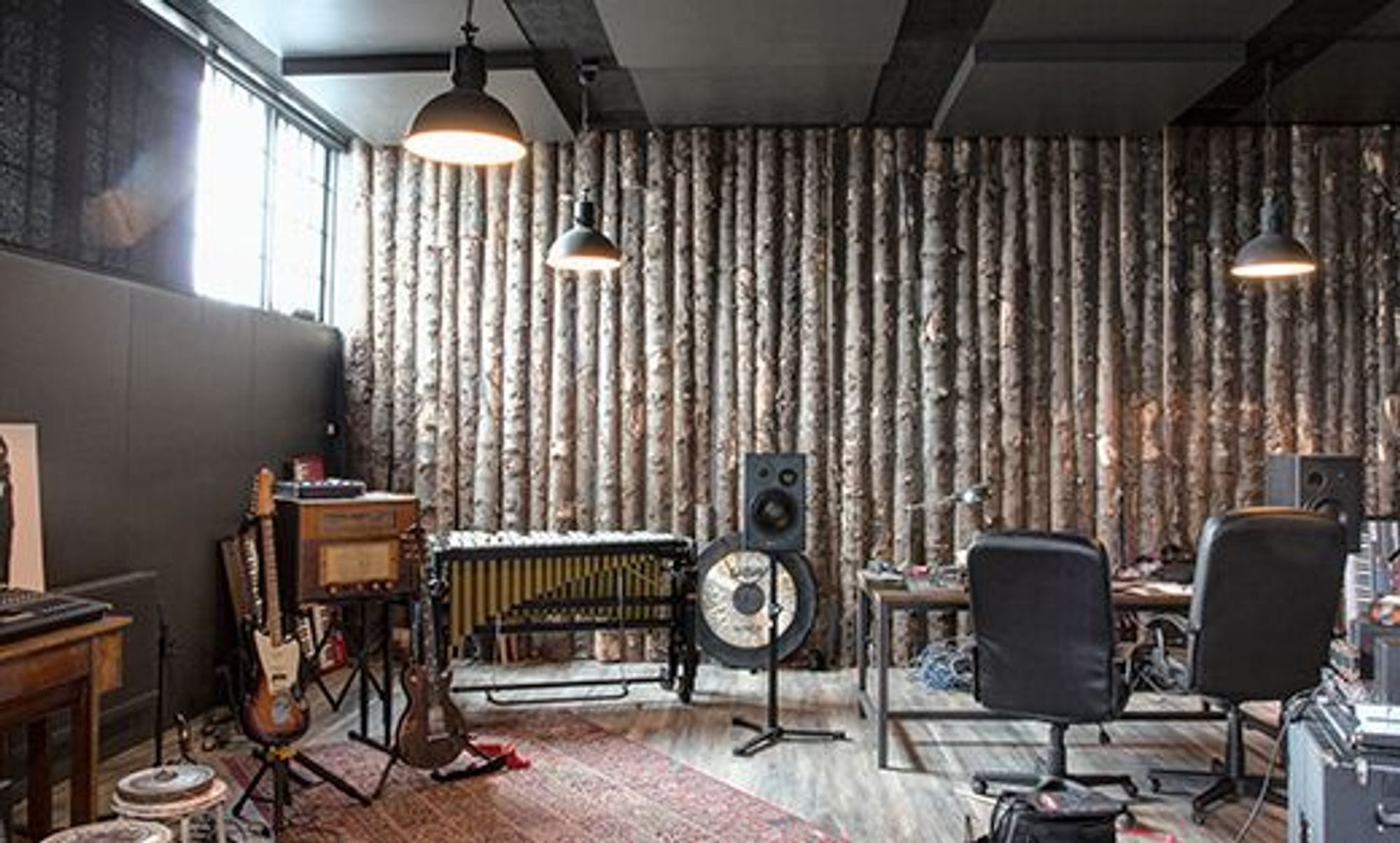 Many instruments and some studio desk and chairs in a studio room covered with raw lumber on the wall