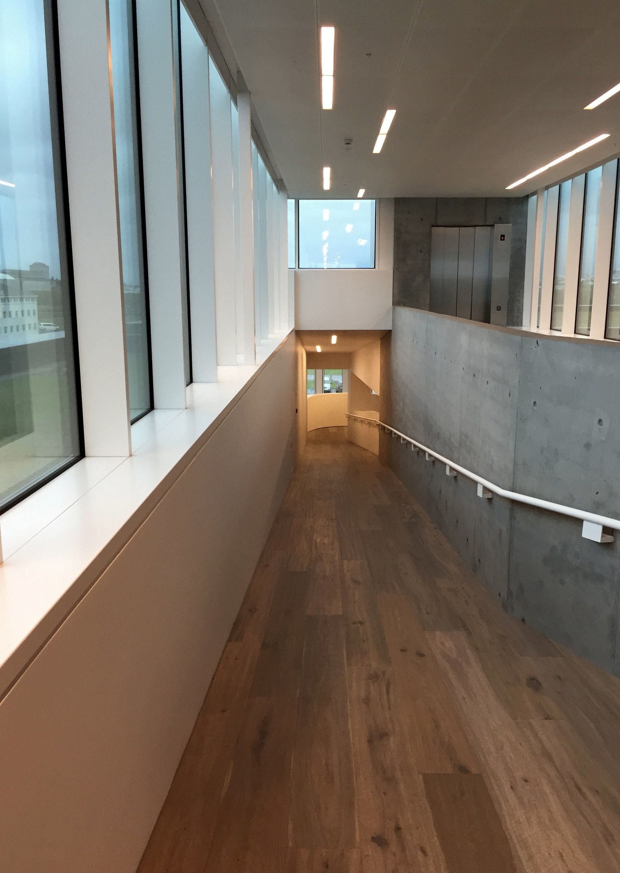 Long sloping corridor with ceiling lighting and windows