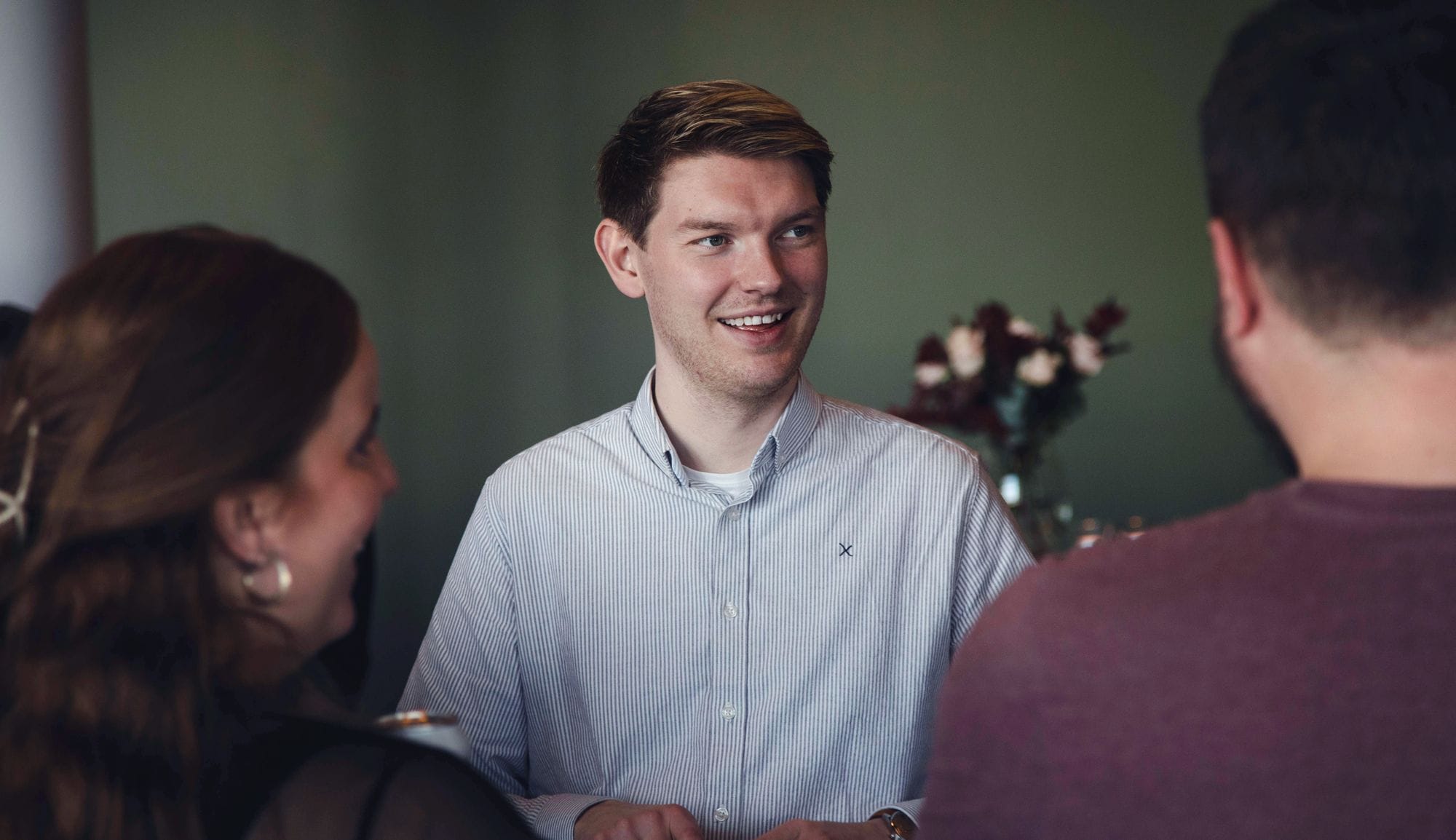 Three people together in a group talking, a man facing the camera is smiling