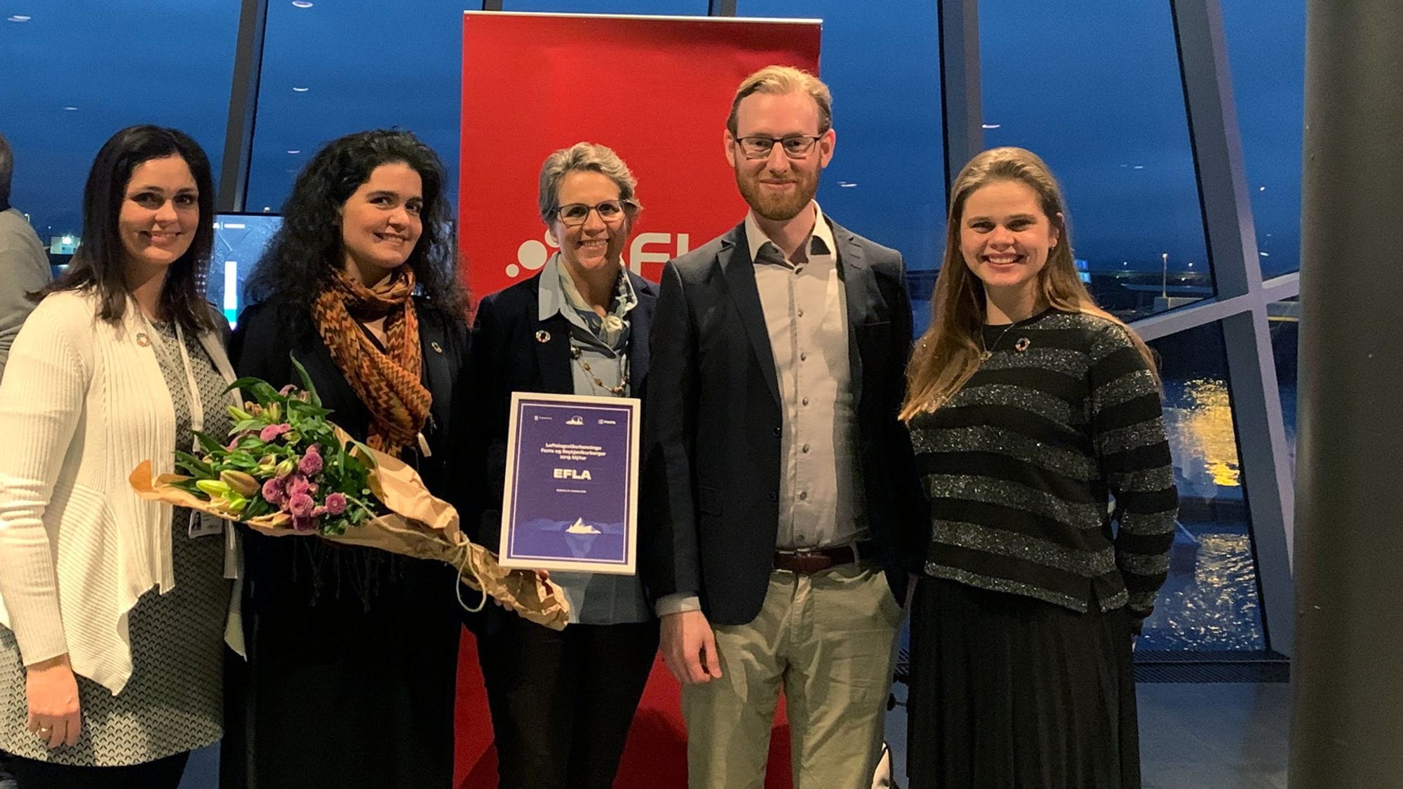 Group of five people holding bouquet and award