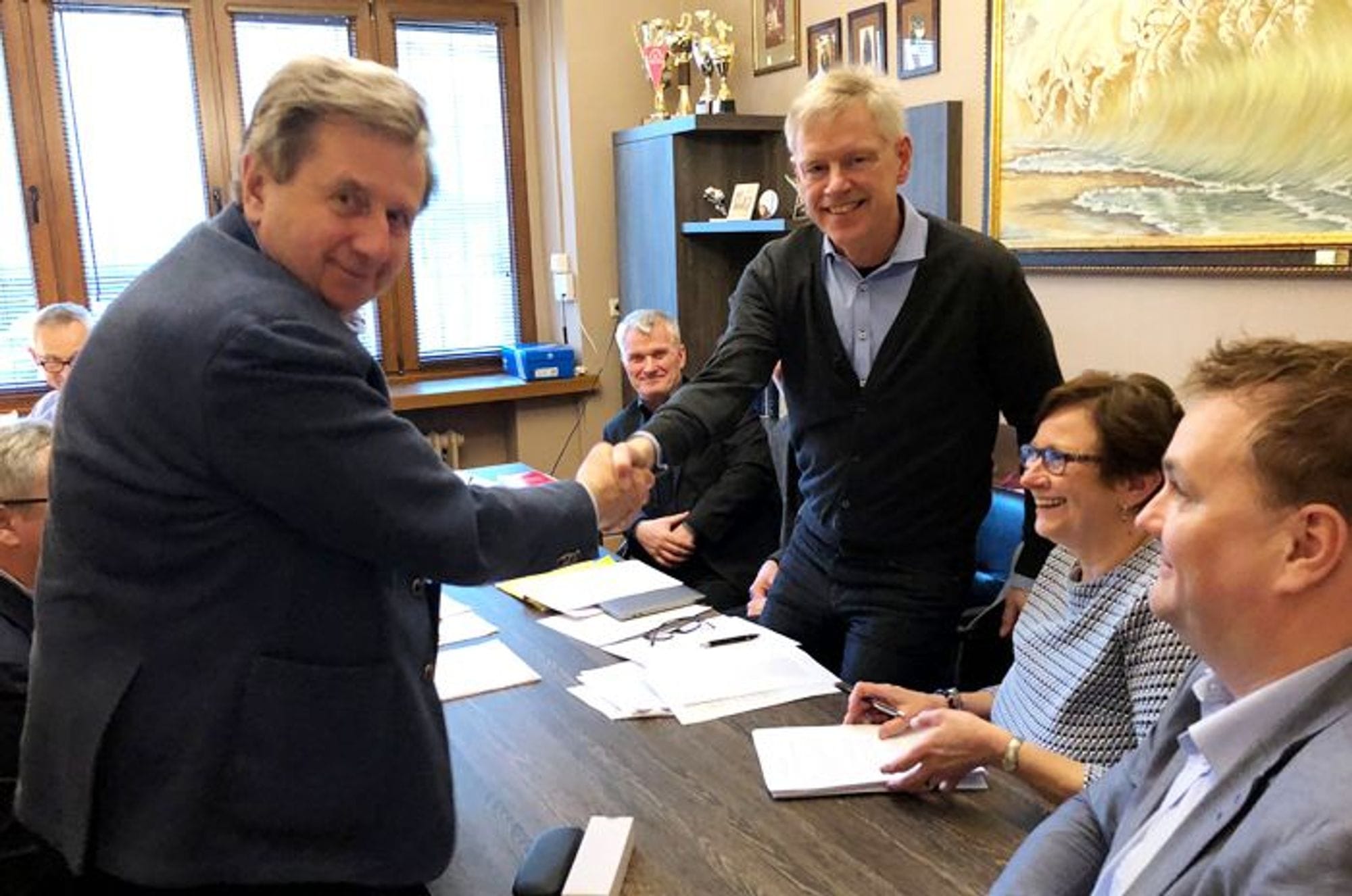 Guðmundur Þorbjörnsson and Marek Dabrowski shaking hands over a meeting table in a room with other people