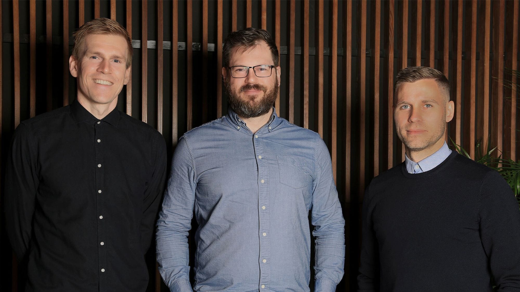 Three men standing, on the background of vertical wood strip wall 
