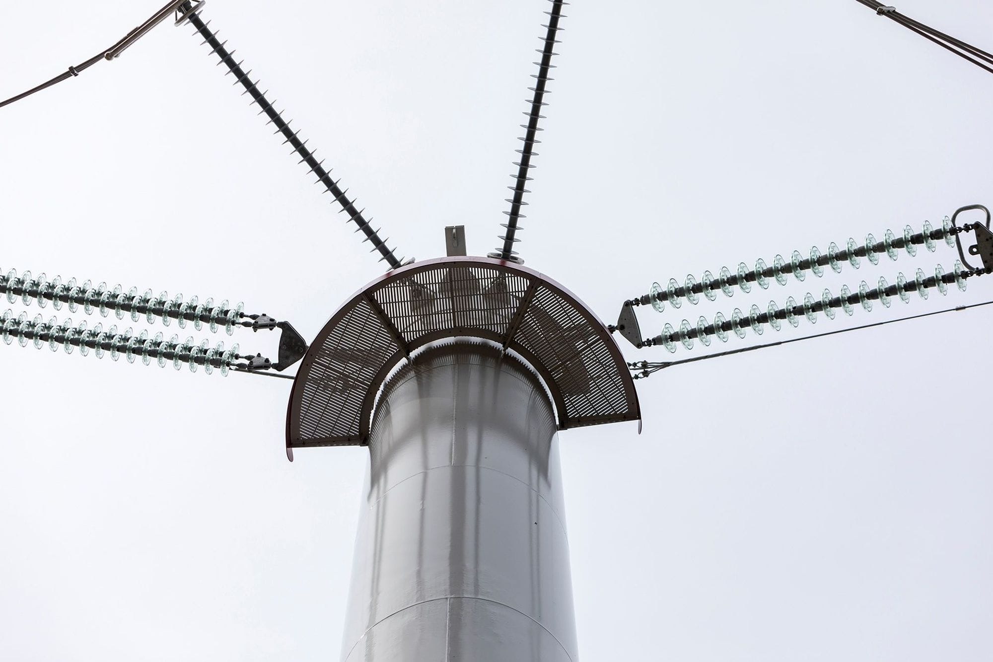 Close-up of a white design mast with black wires extending from the mast in four directions.