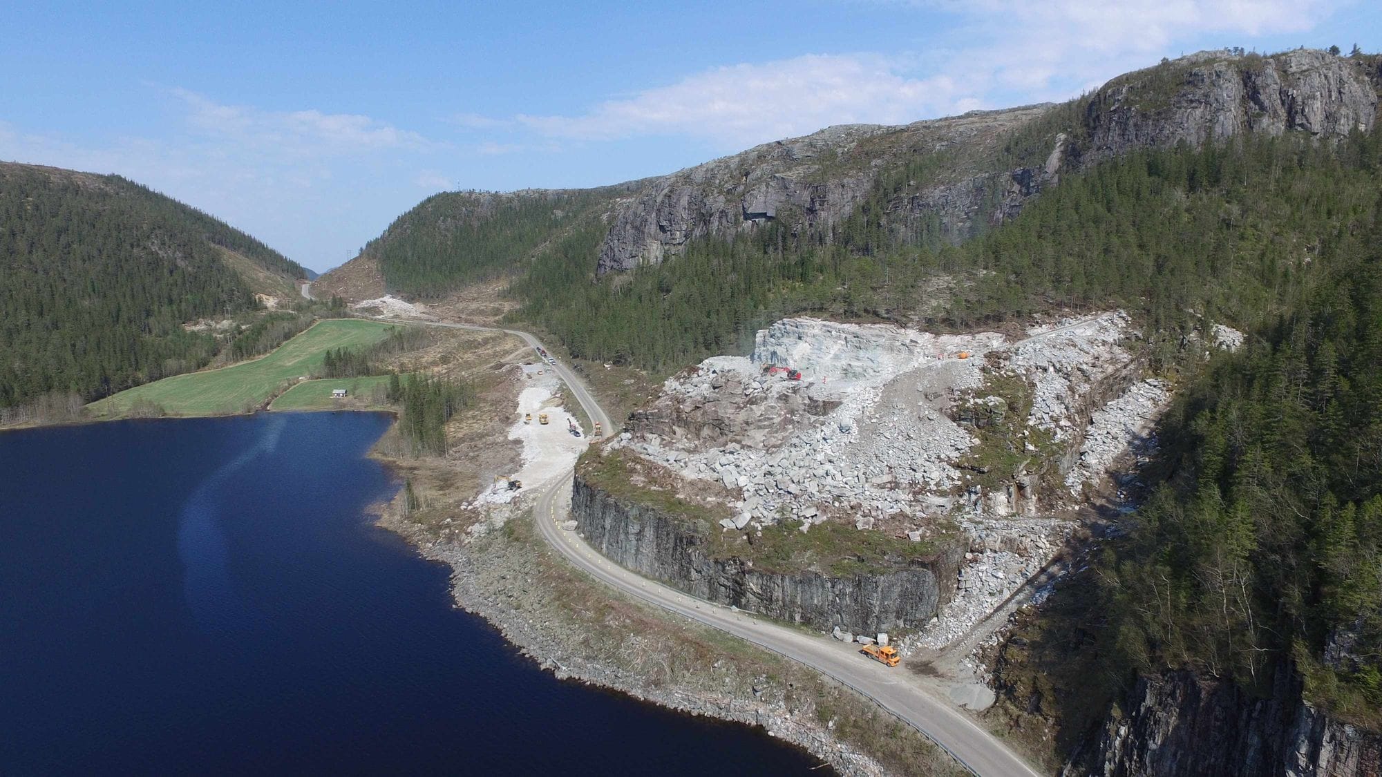 mountains and a lake with a road on the side and construction side above the road in the hills