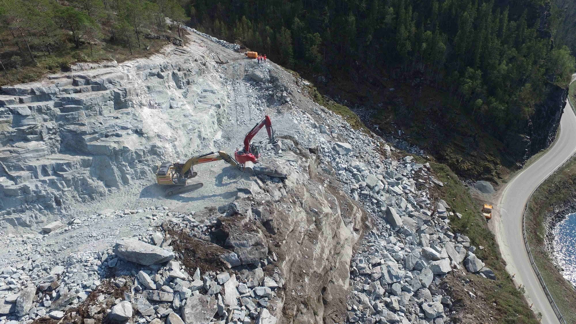 Two excavators working in rough and light grey rocky terrain