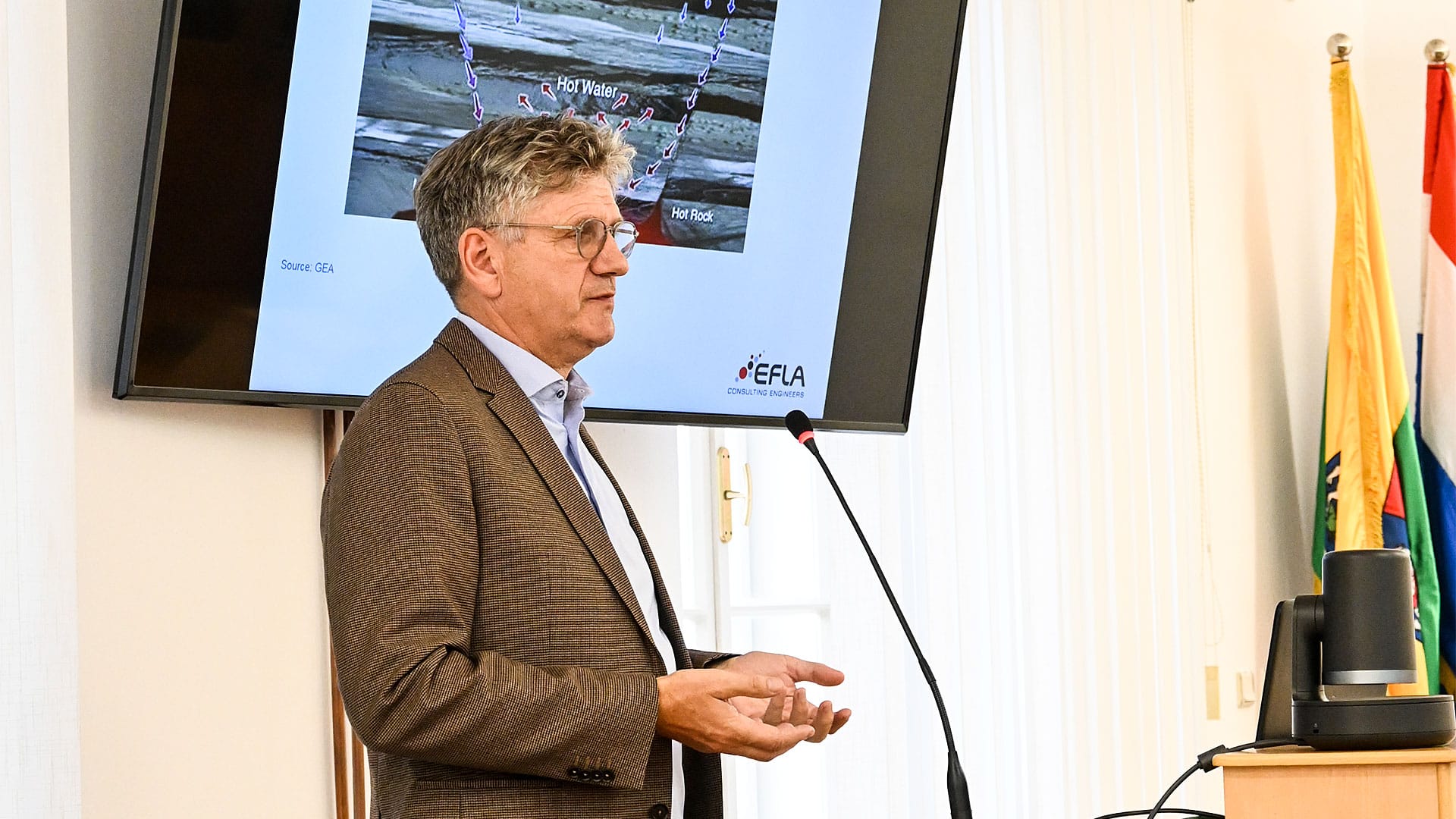 A man giving speech with TV screen at the back
