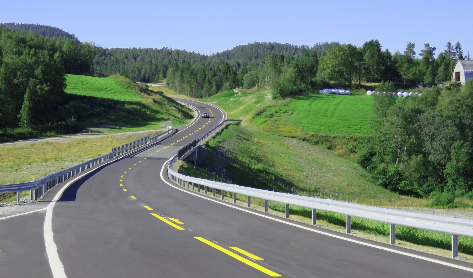 A road winds along grass and woods vegetated land
