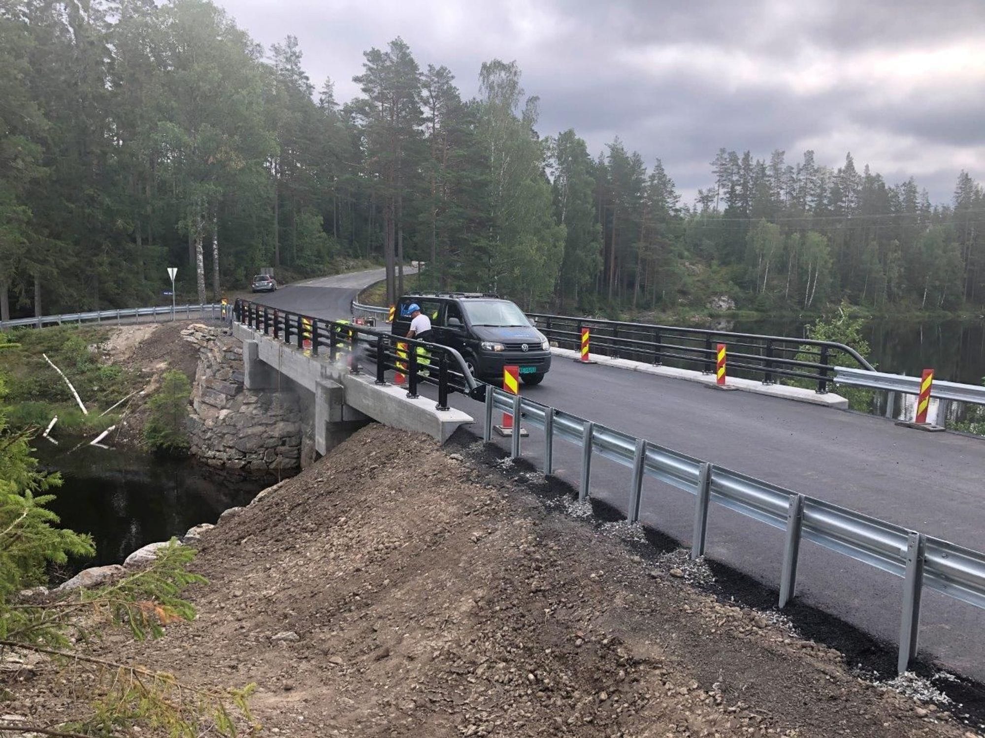 Completion of a new bridge railing on the rebuilt Sunds bridge. Sunds bridge seen from the road, a man in fornt of a car finishes bulding the railing on the nearly finished bridge.