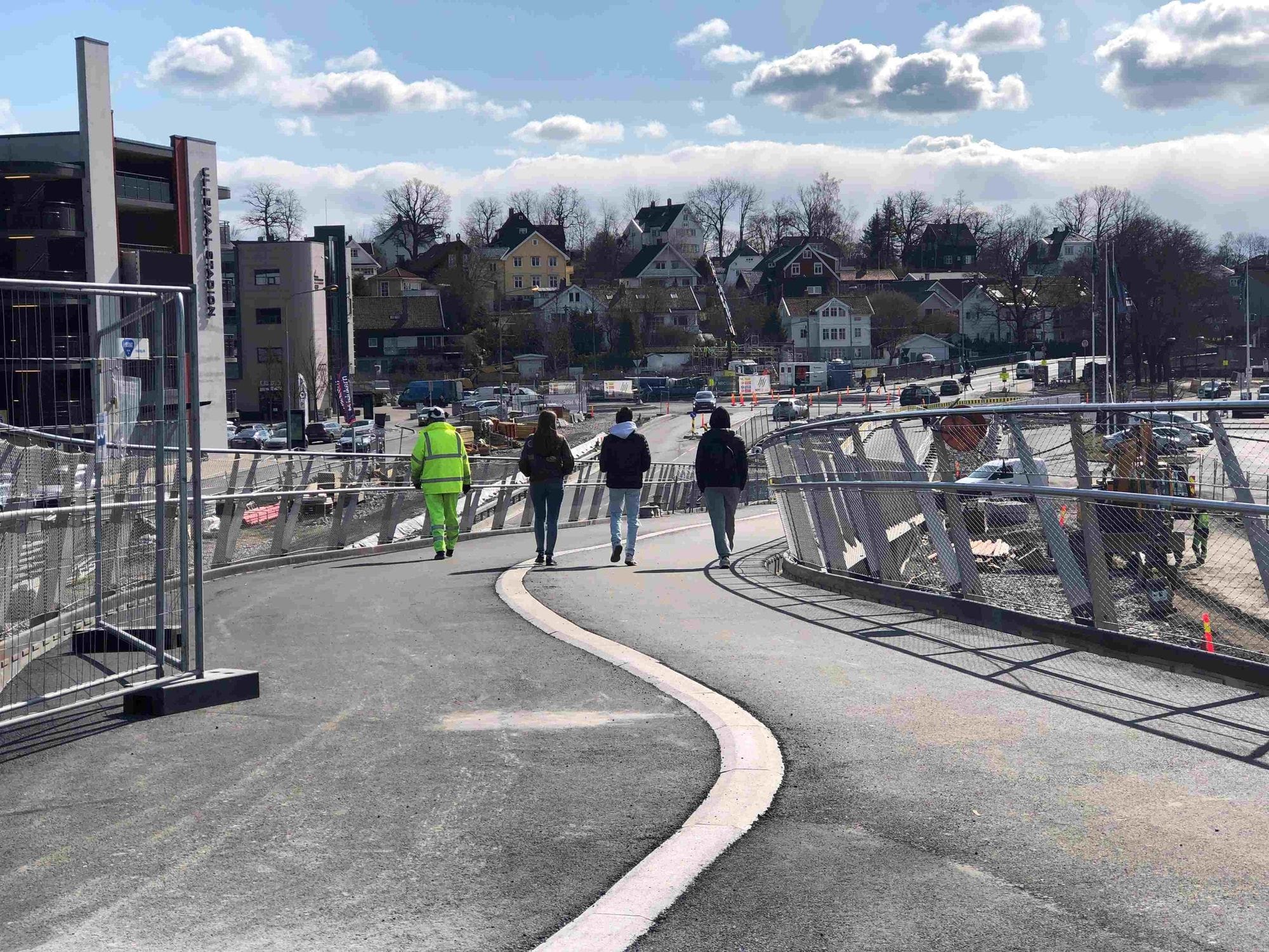 Three people and one man in yellow work clothing walking down a bridge