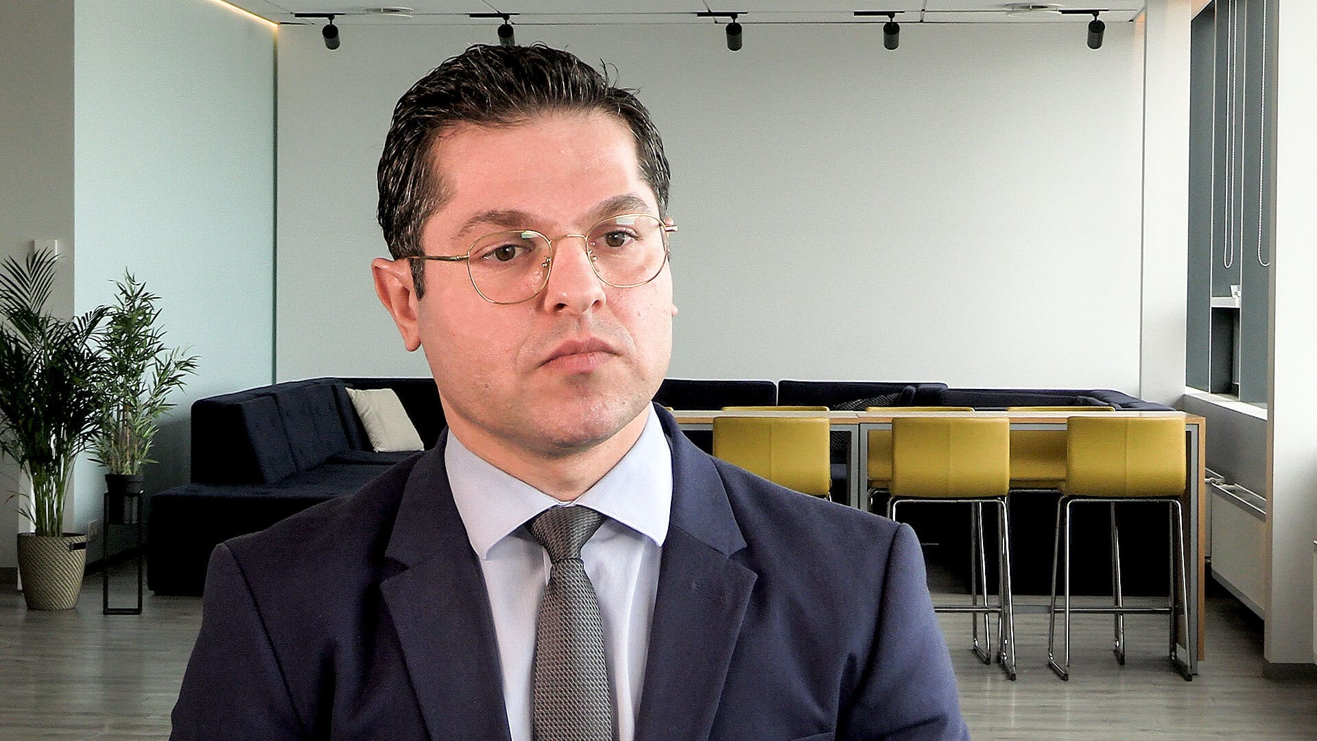 A man wearing dark slate blue suit and glasses
