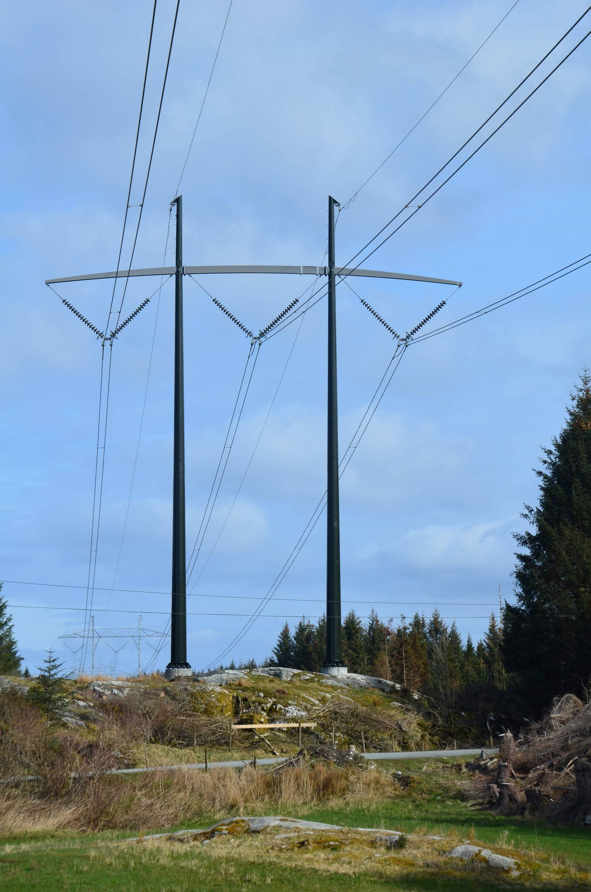 a black mast on top of a lava field and power lines in a blue sky