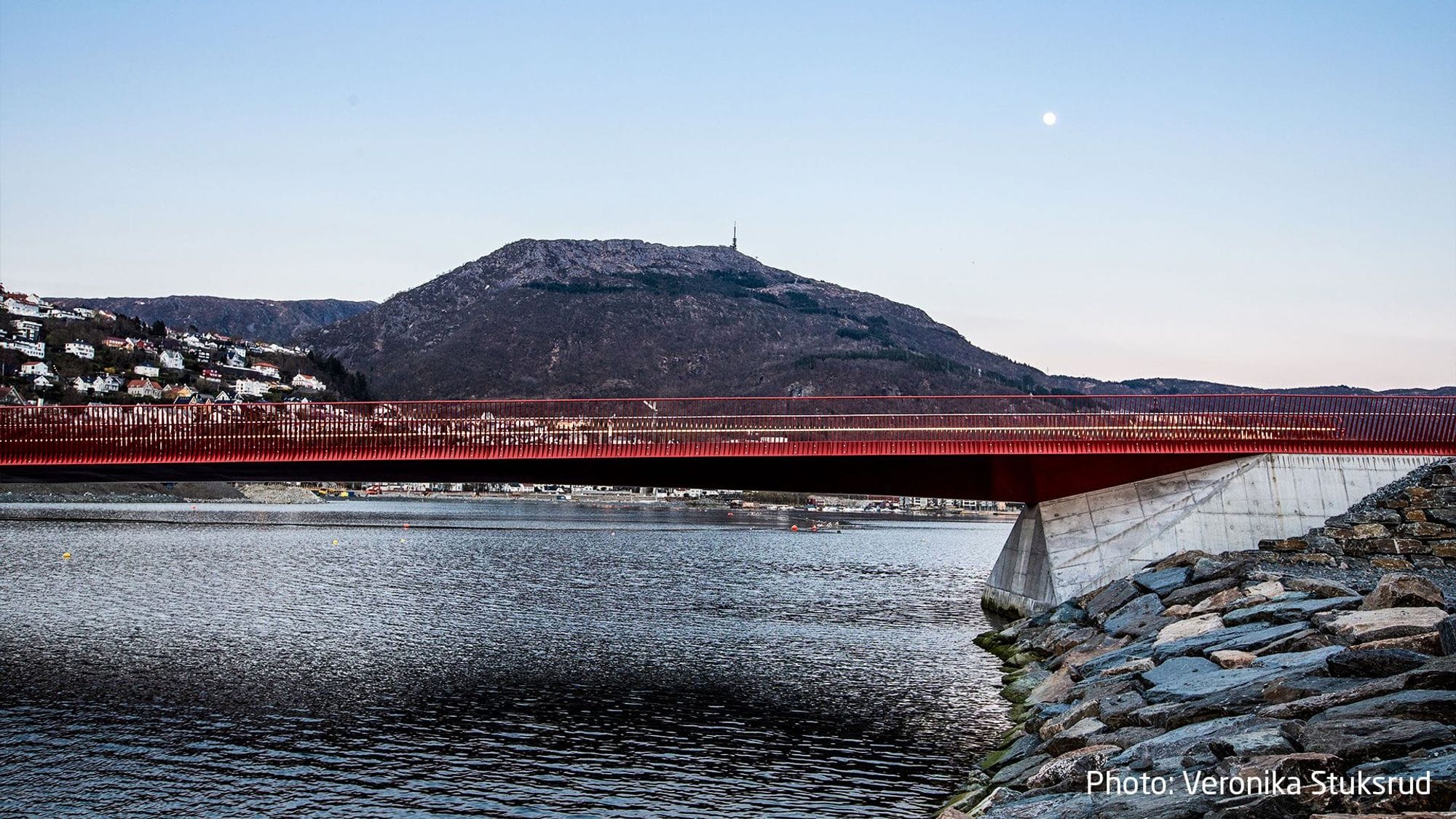 Closeup of a red railing on a bridge with a hill with houses in the background