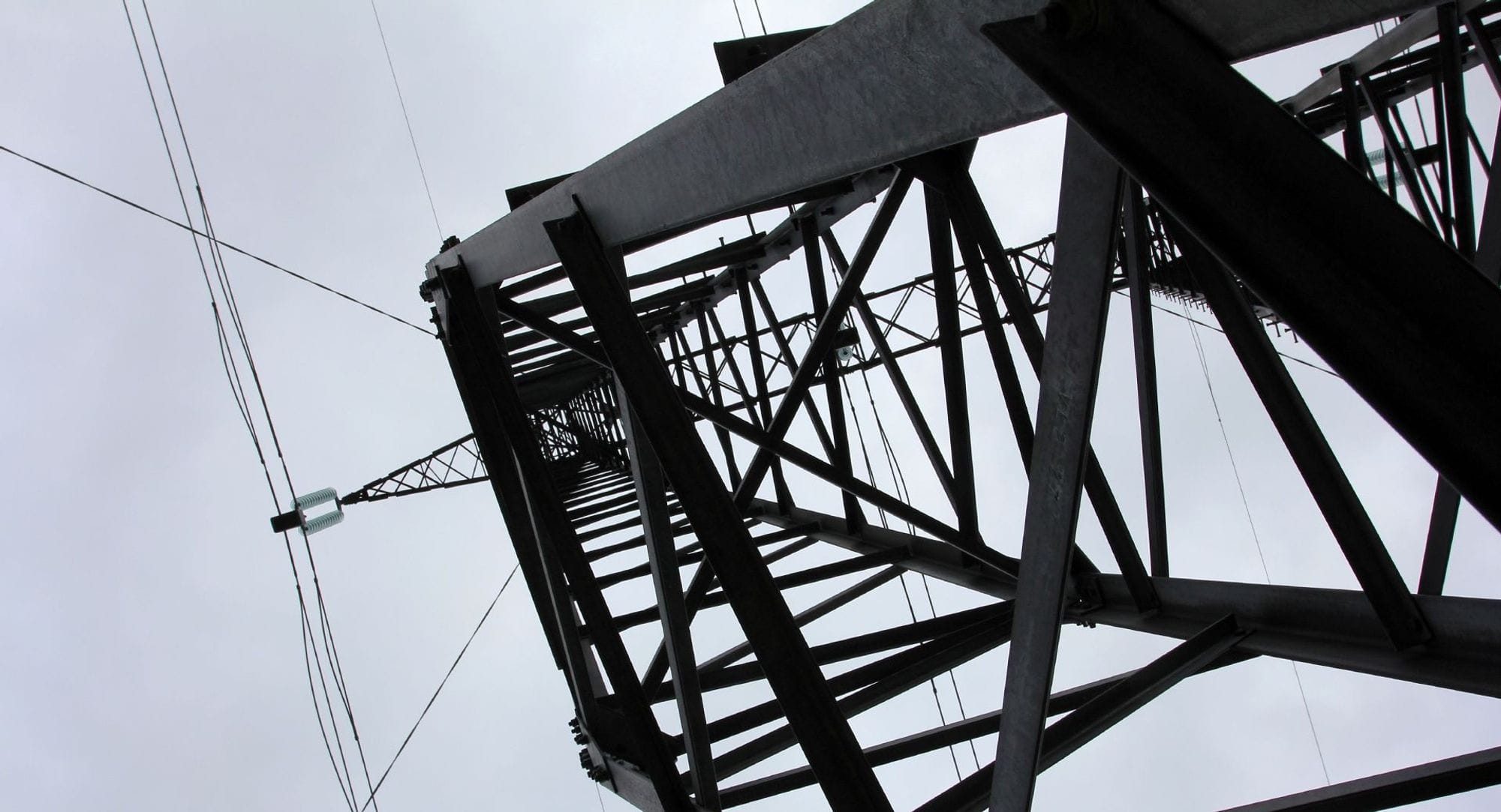 A mast from a viewing angle from below and up towards a greyish sky, there are tension lines running from the mast