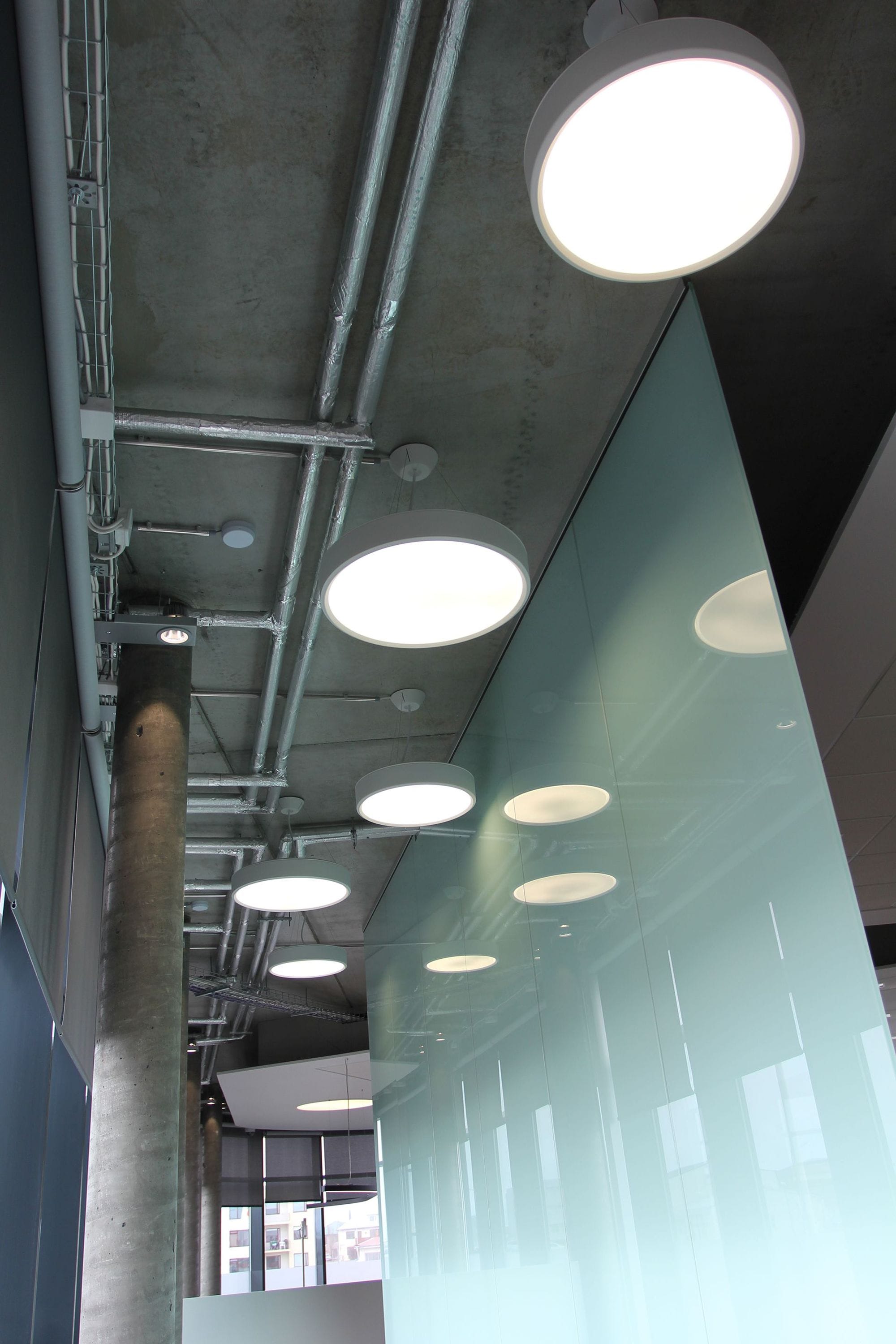 Modern lights in the ceiling of a concrete building with a glass panel on the right
