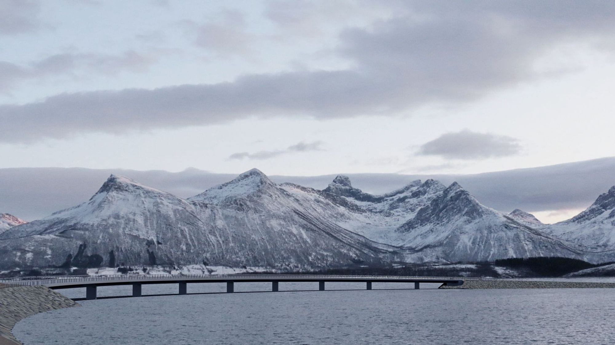 A long bridge over an open water, snow covered mountains in the background