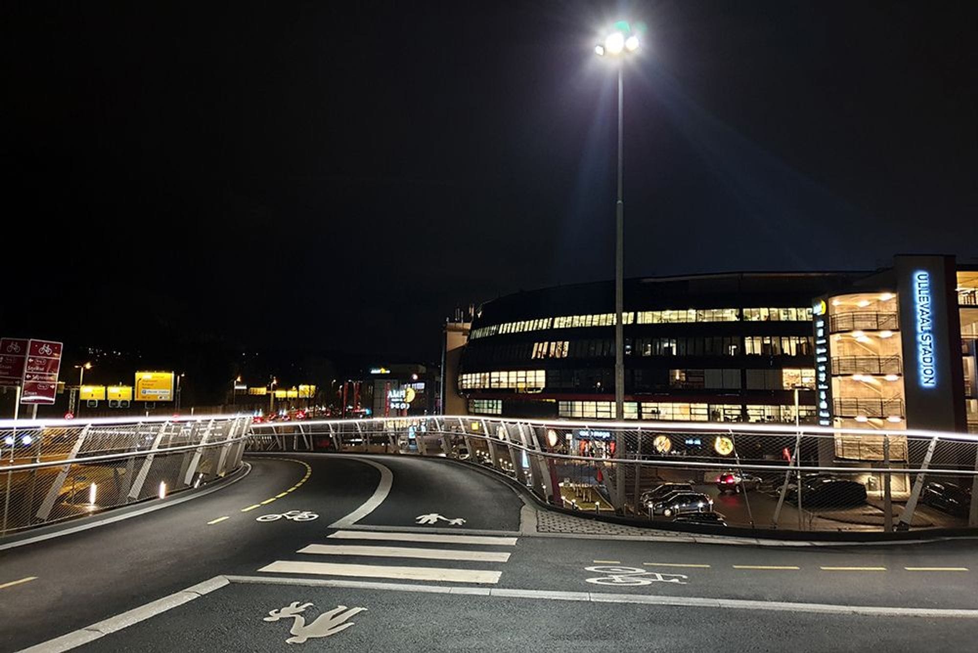 A bridge with an intersection showing signs for pedestrians and cyclists in a dark environment