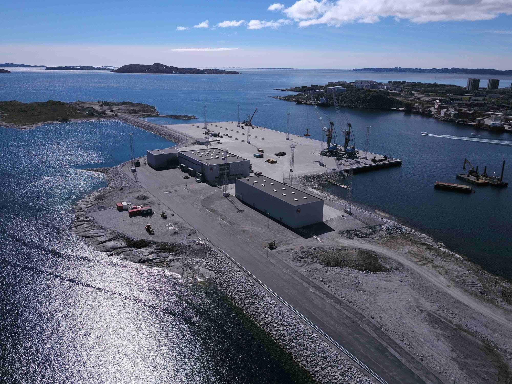 Large boat port seen from land with big buildings on it, cranes and surrounded by the sea