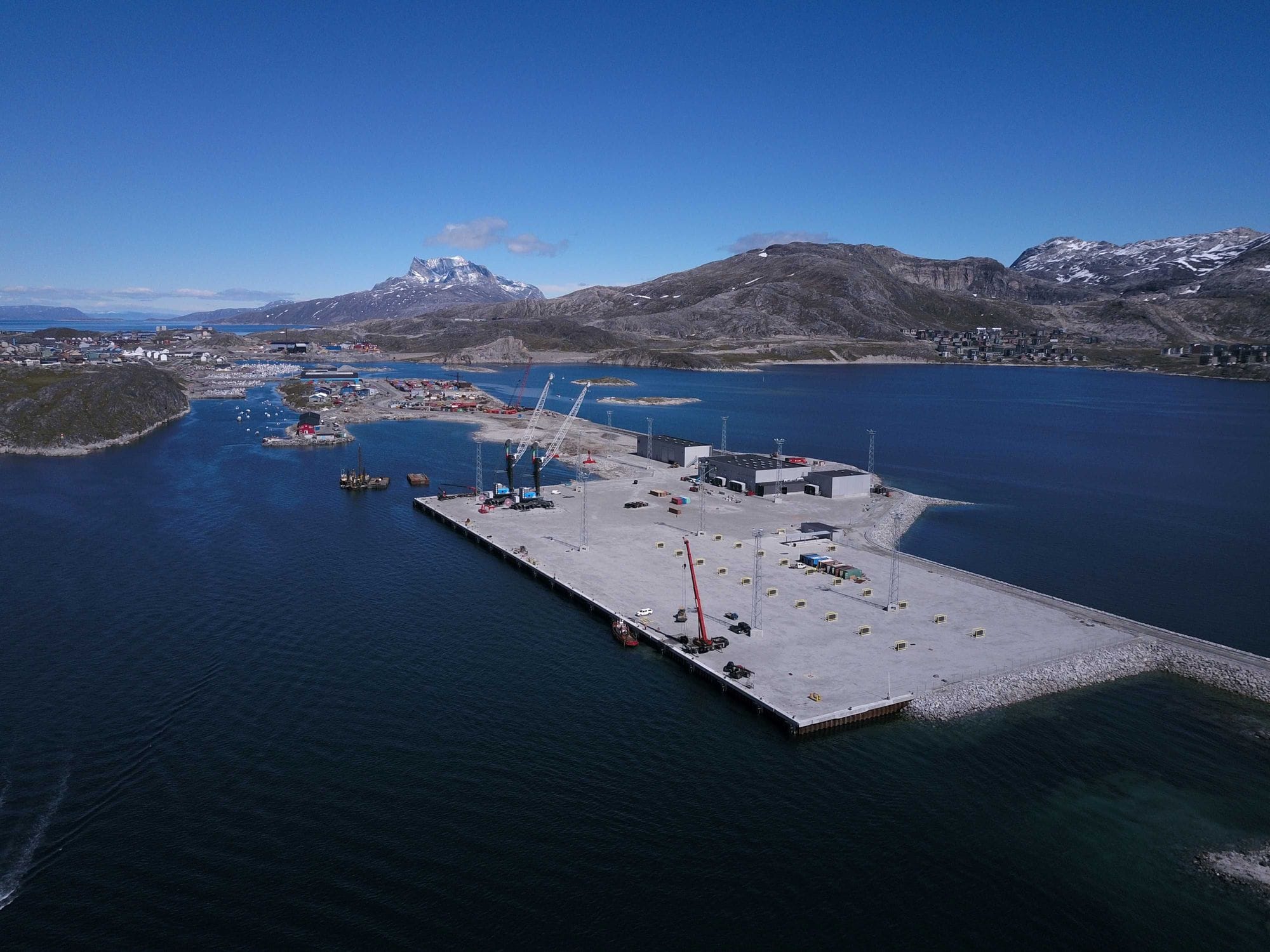 Large boat port seen from above with big buildings on it, cranes and surrounded by the sea and mountains