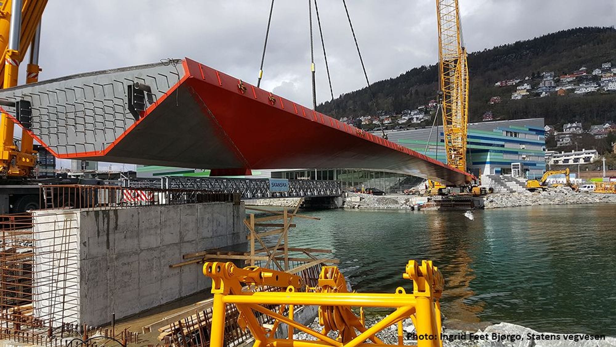 Yellow crane lifts red steel bridge and locates over sea