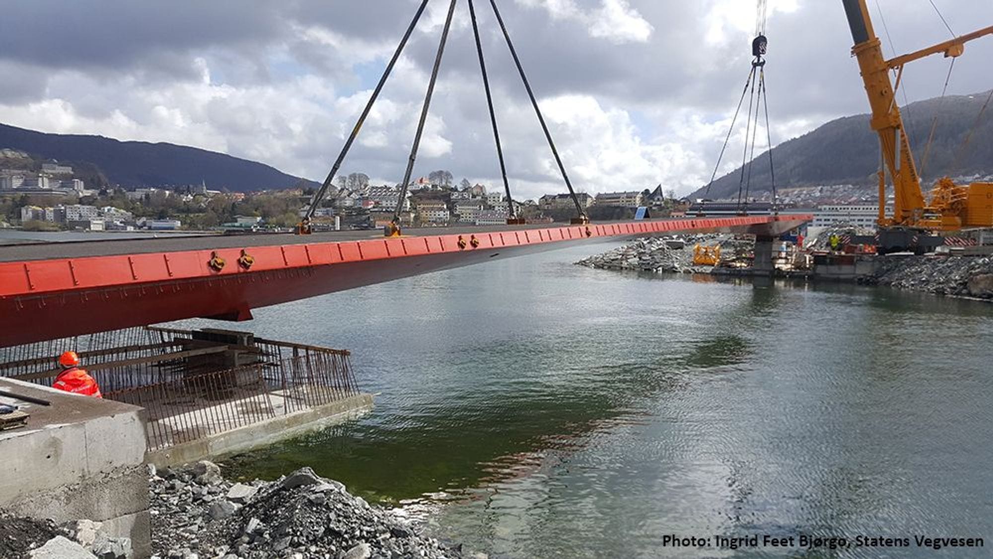 Yellow crane lifts red steel bridge and locates over sea