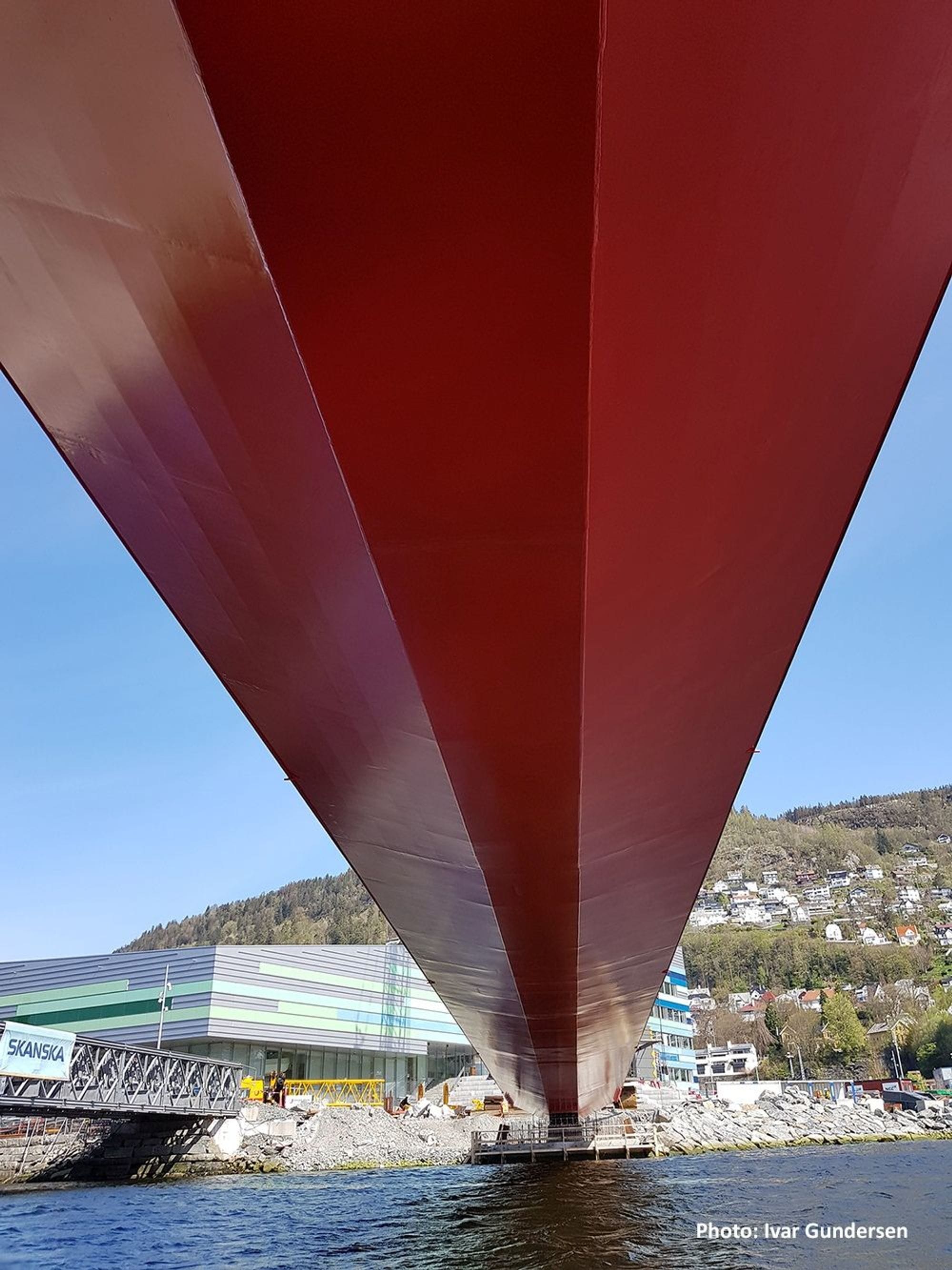 Red steel bridge in close  up from under showing it ending on land and buildings and trees in the background