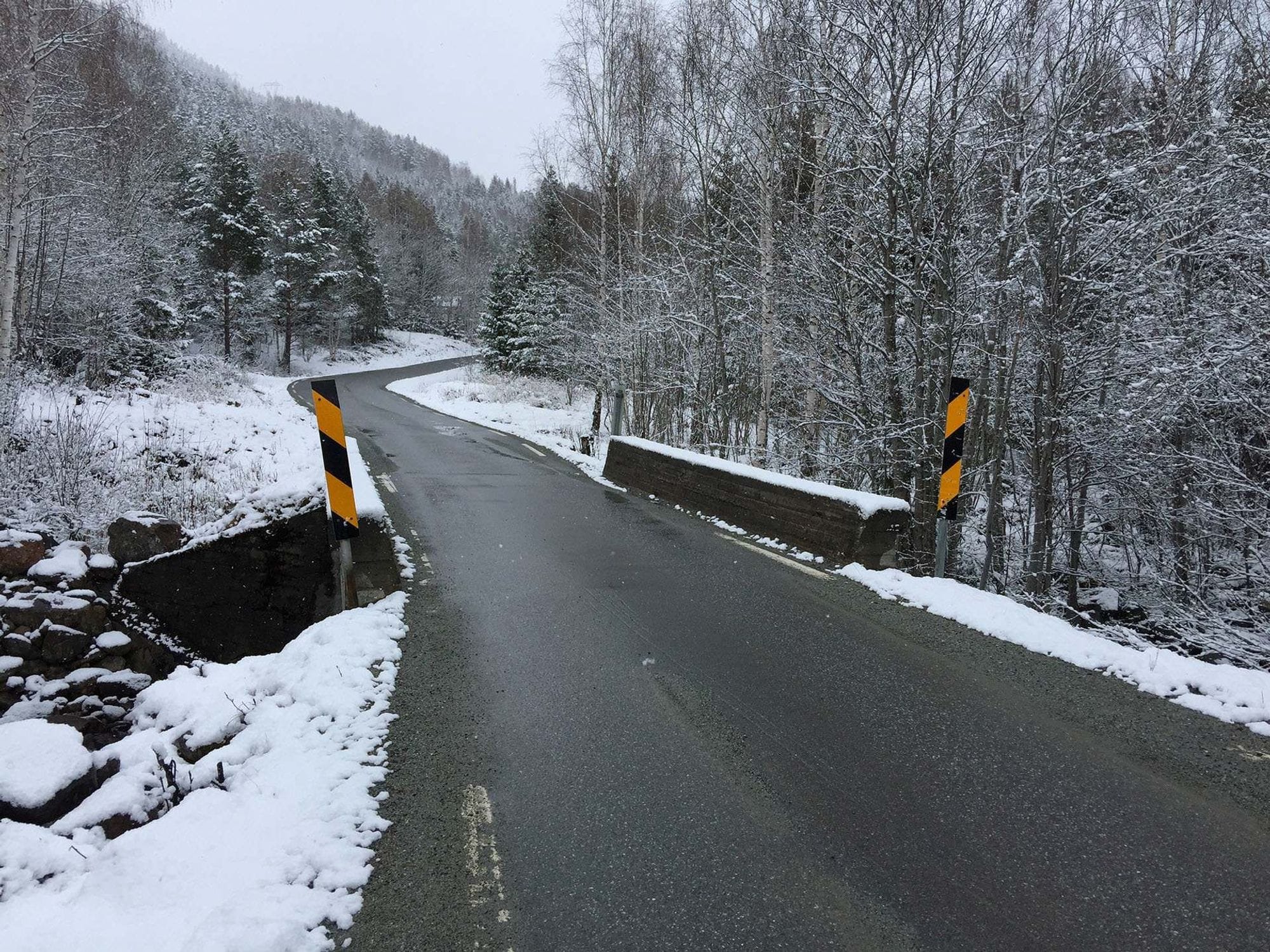 Velta bridge befor rehabilitation. No steel rails, but low concrete rails on the edge of a really narrow bridge. Snowy surroundings and forest.