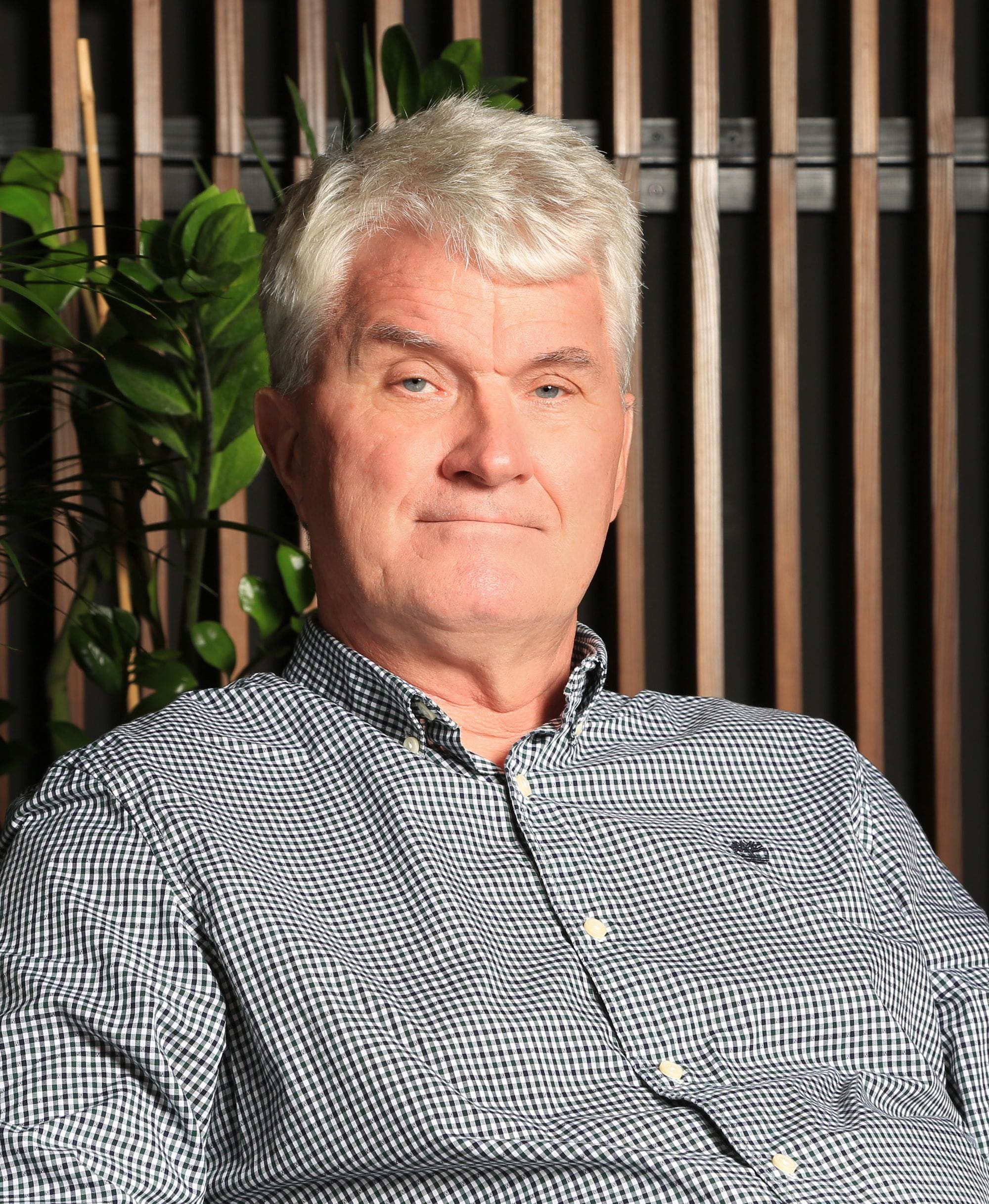Portrait of a man, green plants and wooden panel in background