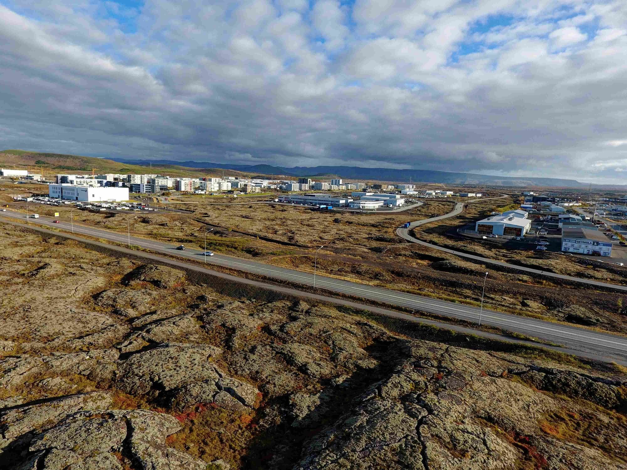 Overview of a populated area surrounded by lava fields, picture showing one straight road passing the buildings