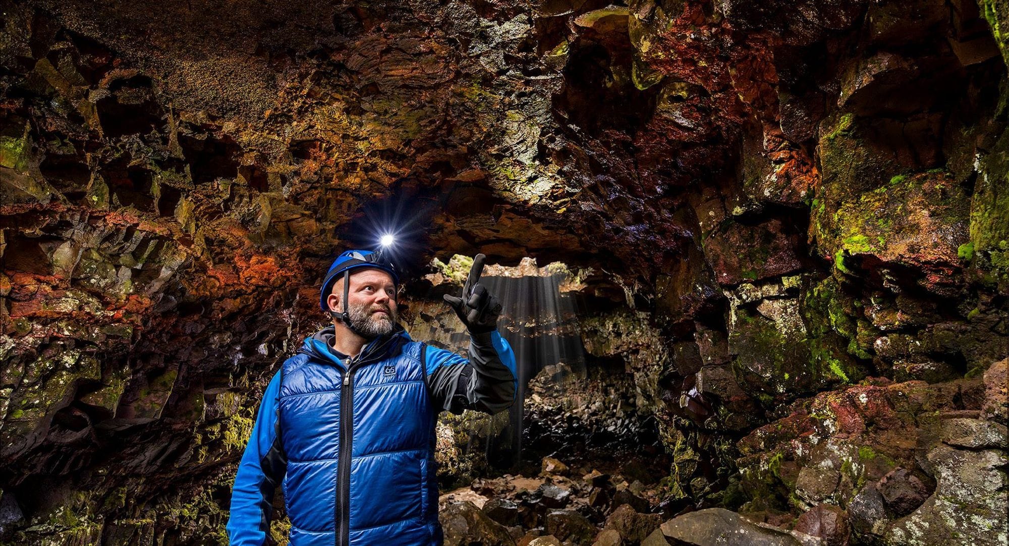 A man in a cave wearing a blue jacket and blue security helmet with light on