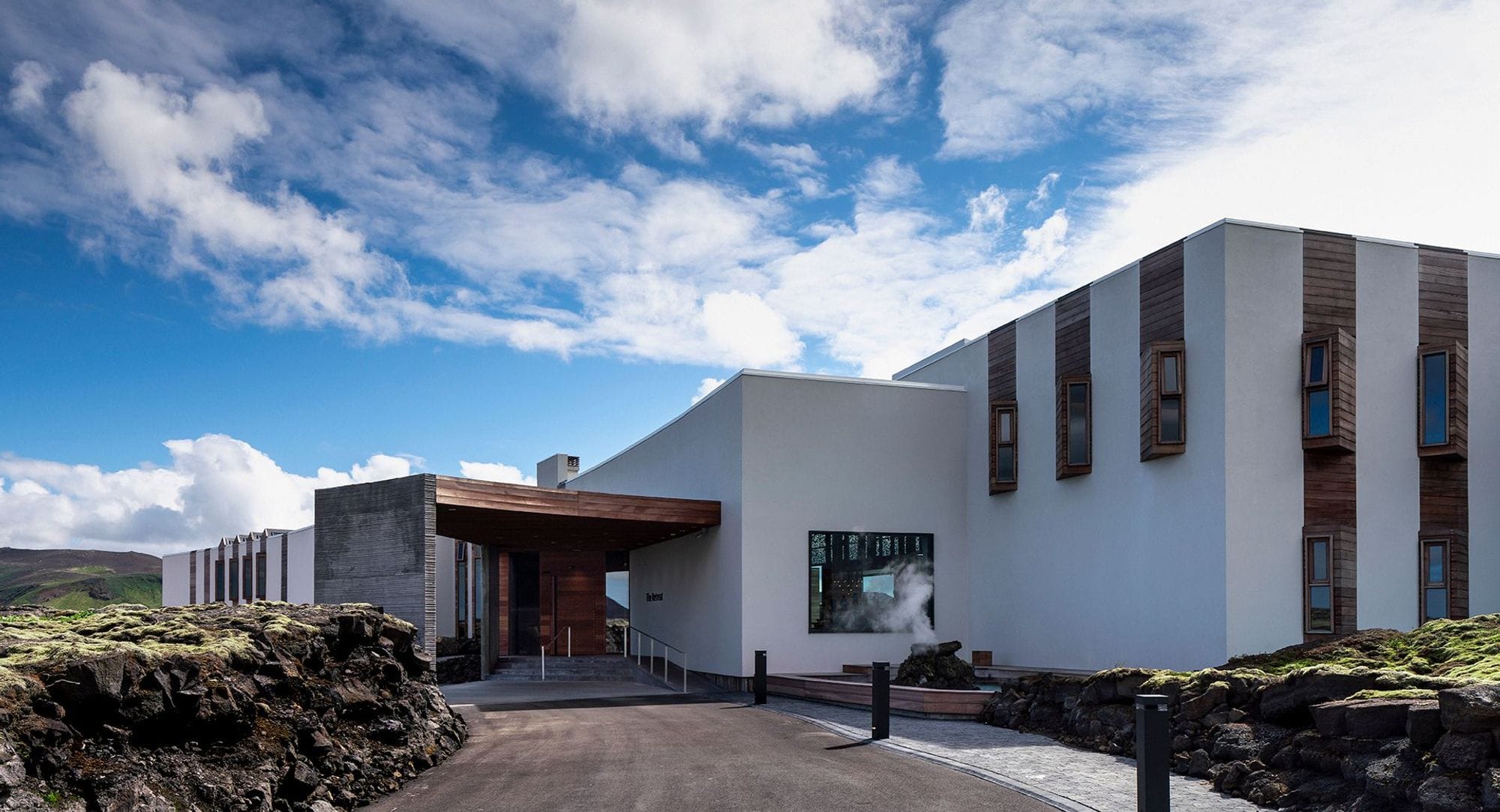 The entrance of the blue lagoon, a white box structured building and the entrance is made of concrete and wood, lava around 