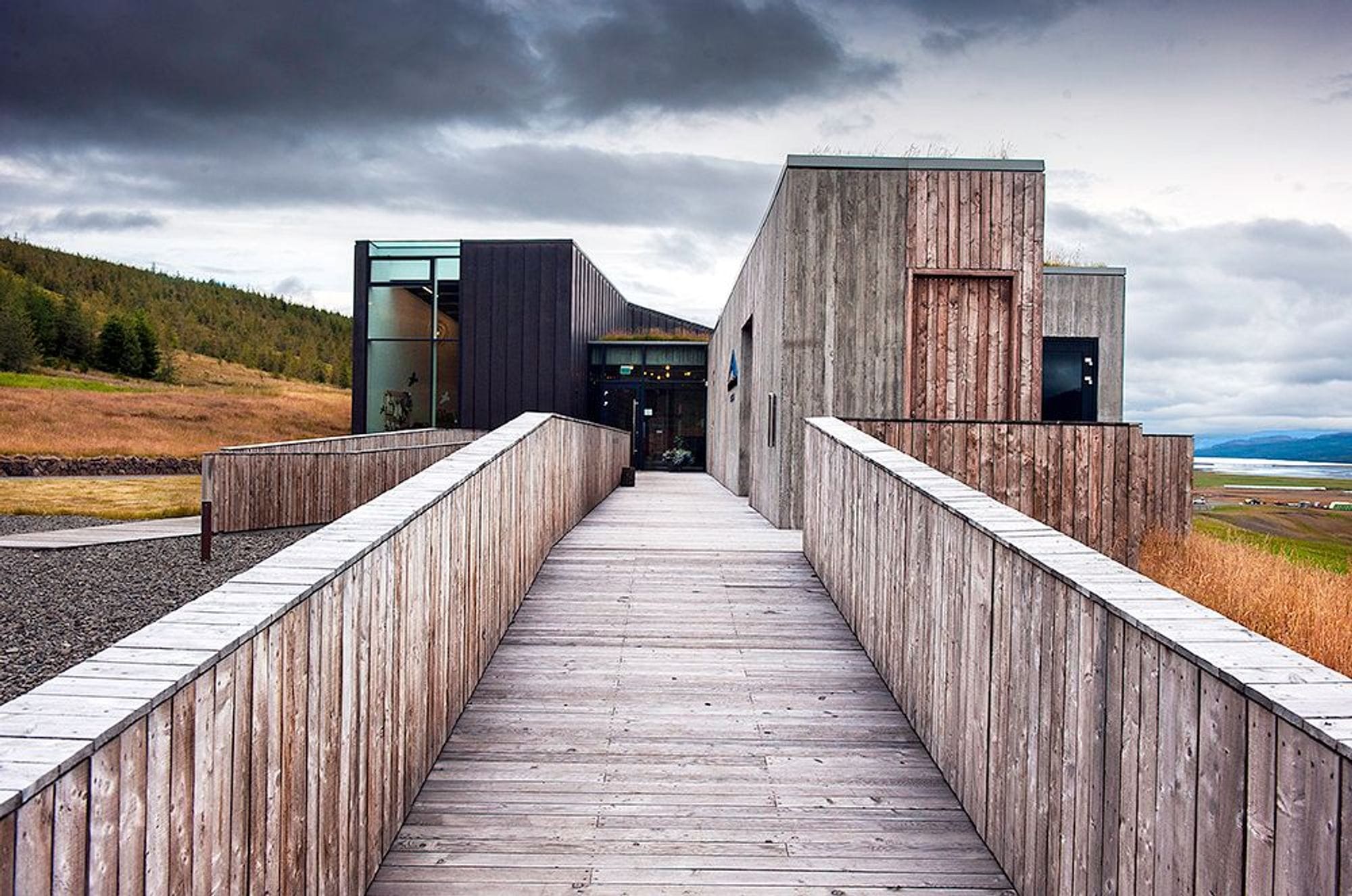 Picture of Snæfellsstofa seen from the entrance. The house is built of box-shaped structures and some are clad with raw wood panels and parts with black cladding. 