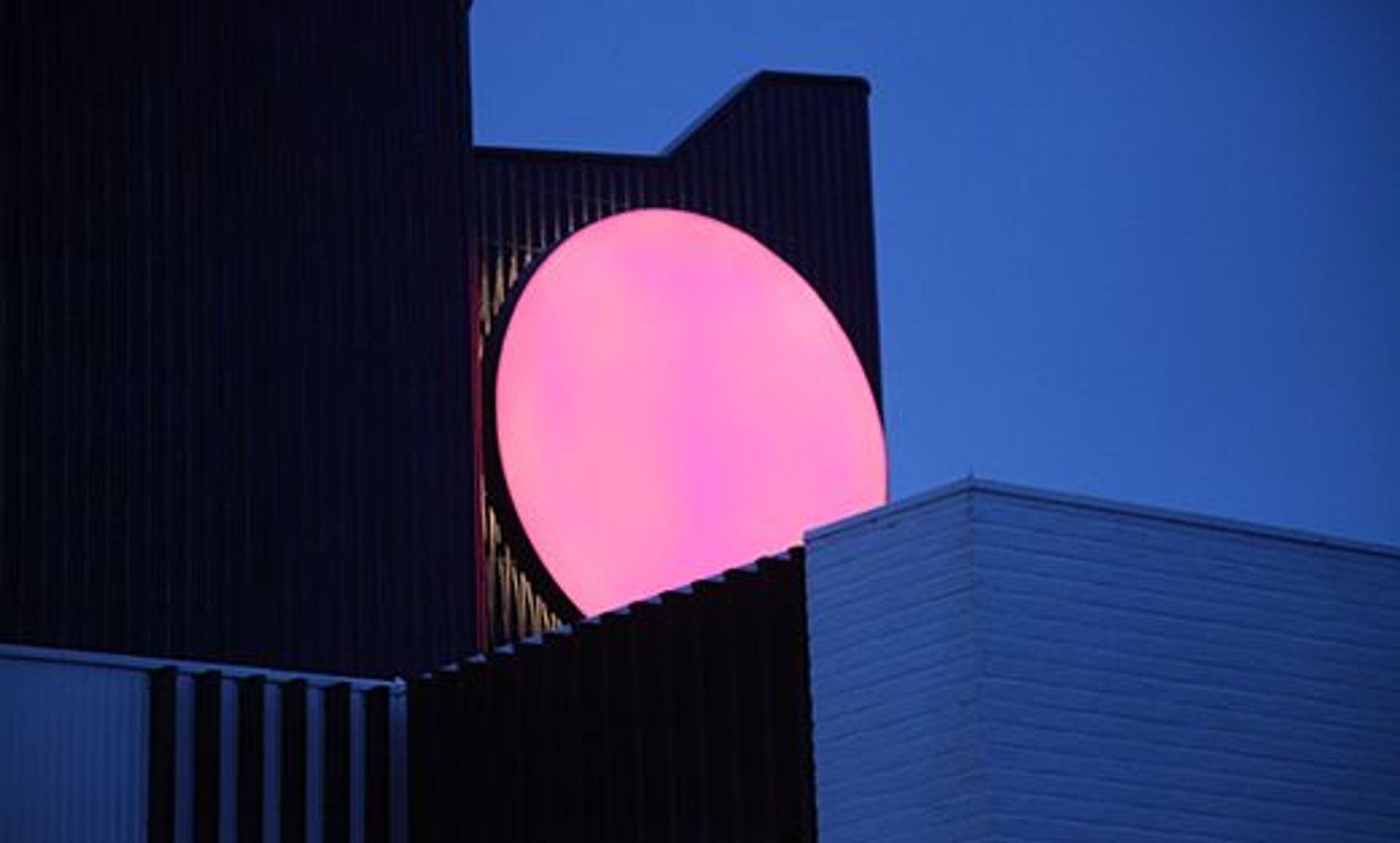 Travelling sun, a big rounded light sculpture with on a wall of a building in the dark