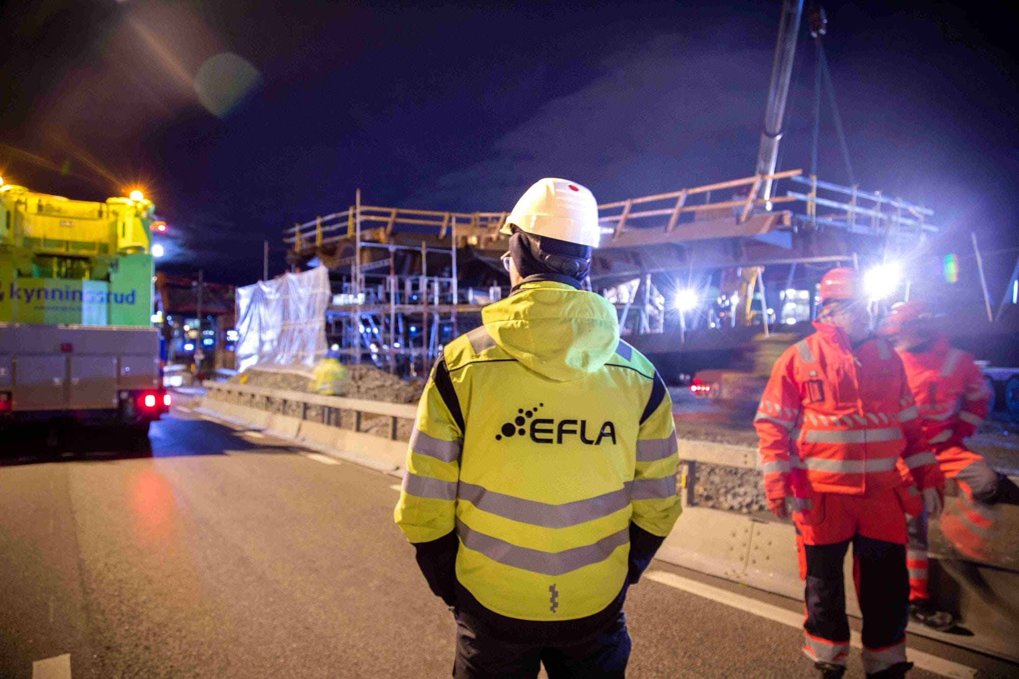 Picture of the back of a man standing in a construction side wearing a white security helmet and a yellow working jacket with EFLA logo on the back.