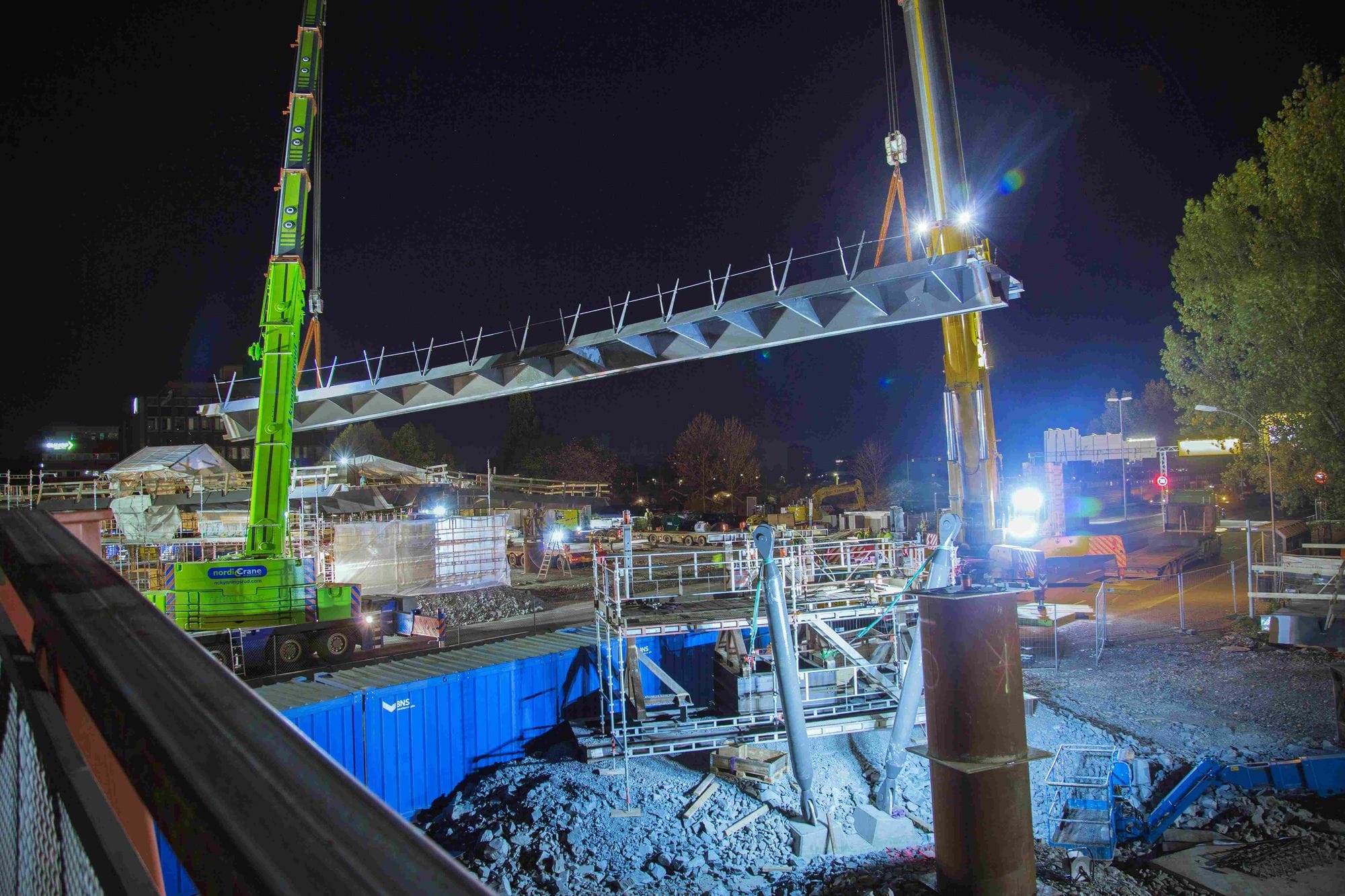 Heavy elements of a bridge being assembled by cranes on construction side by night