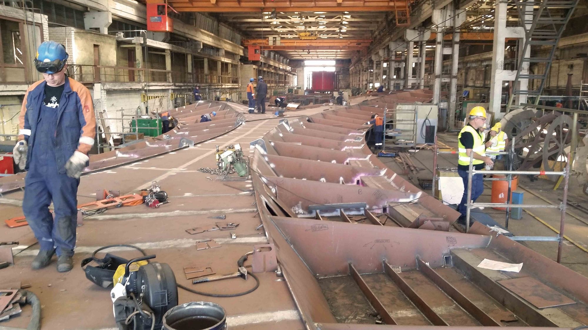 two of 16 parts of the bridge being built and laid out inside a construction workshop, men working on the building workshop