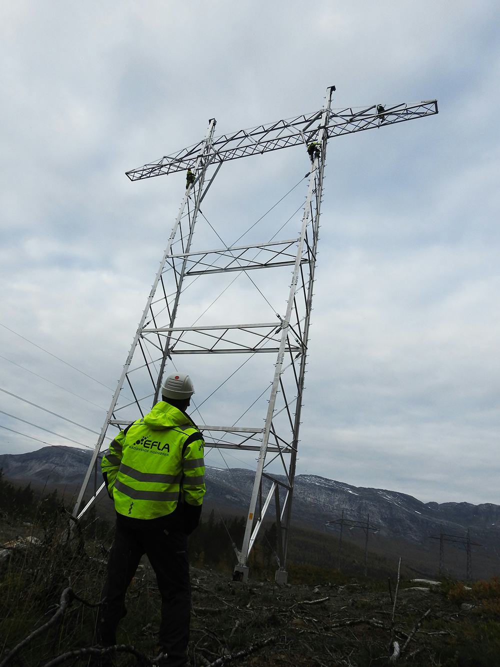 A man wearing EFLA construction jacket glancing at a transmission tower