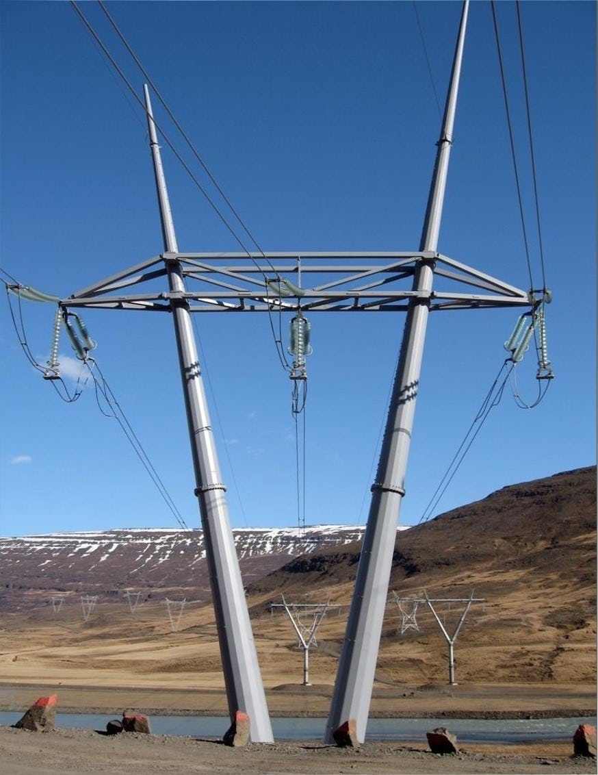 A vertical shot of transmission tower under blue sky, several look alike towers and mountain in the background 