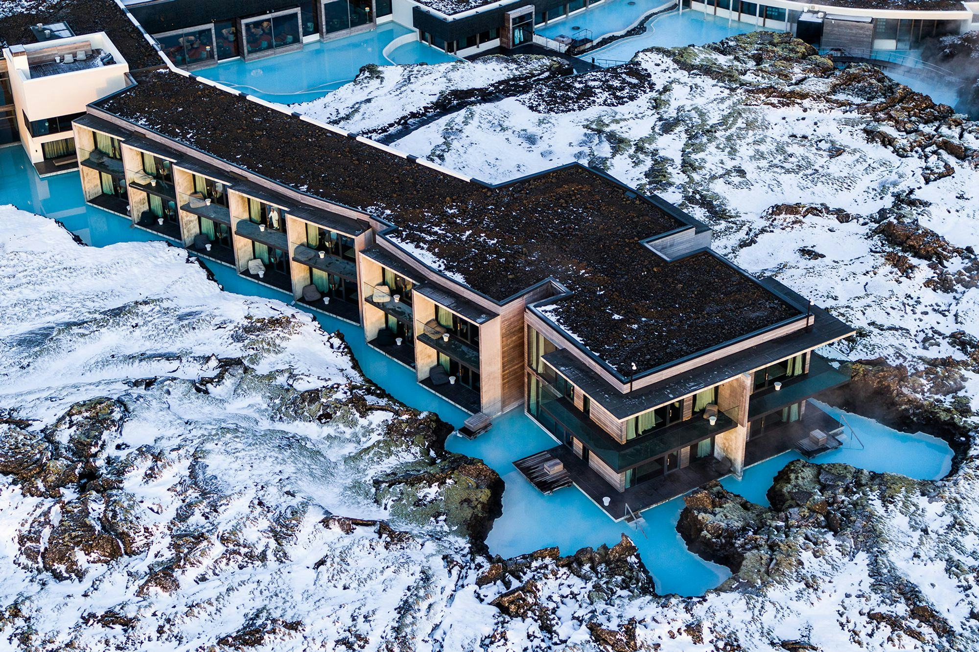 Aerial view of a long modern building in the middle of a lagoon, snow covered lava all around