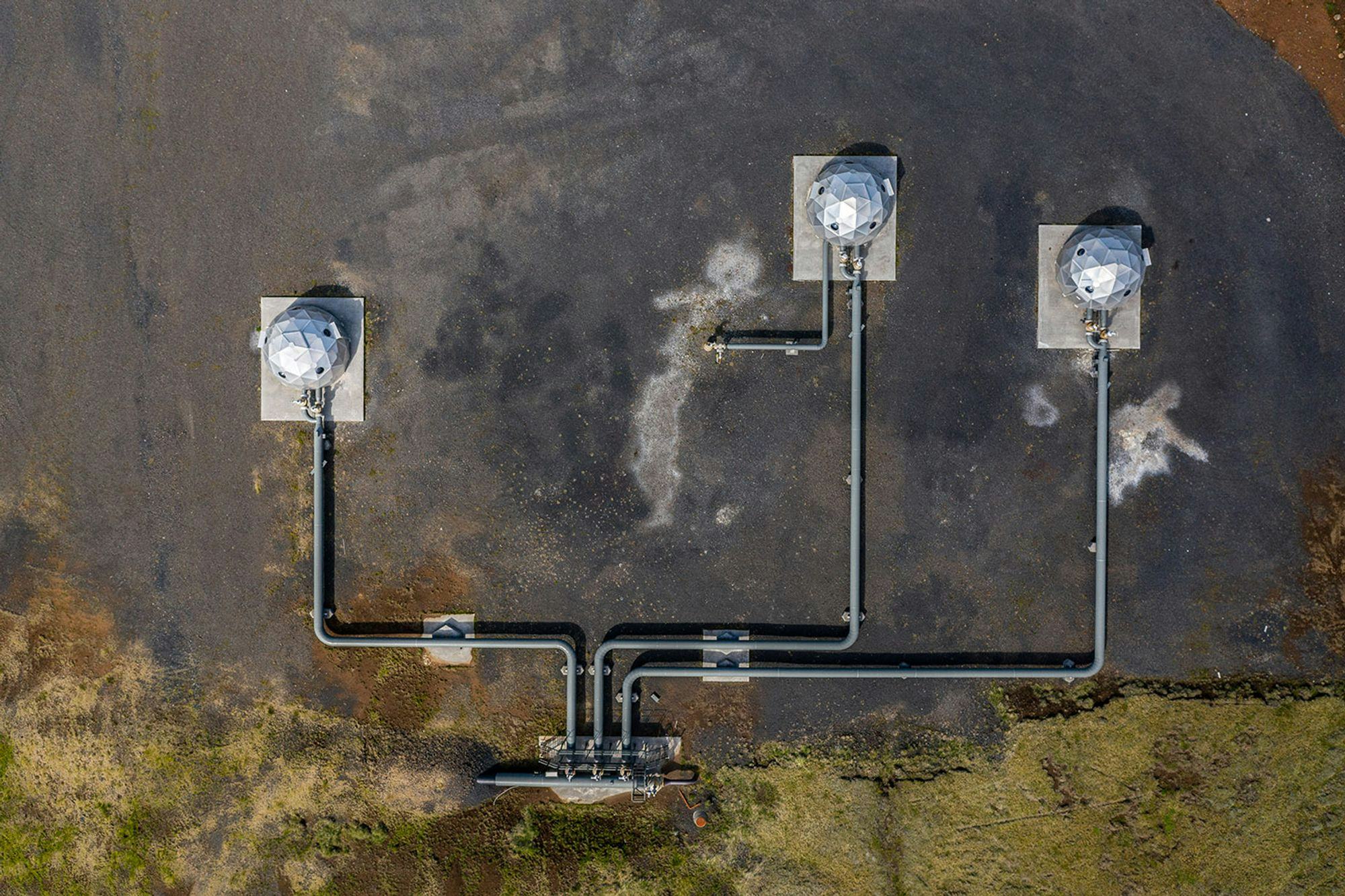 Aerial view of some kind of industrial plant, three buildings that are globes connected by pipes, on gravel, moss around the gravel