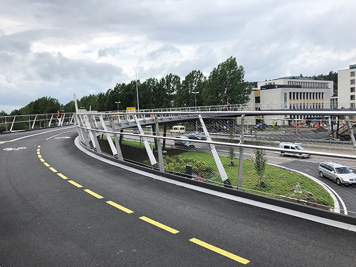 cars cruising under a footbridge with silver metal railing