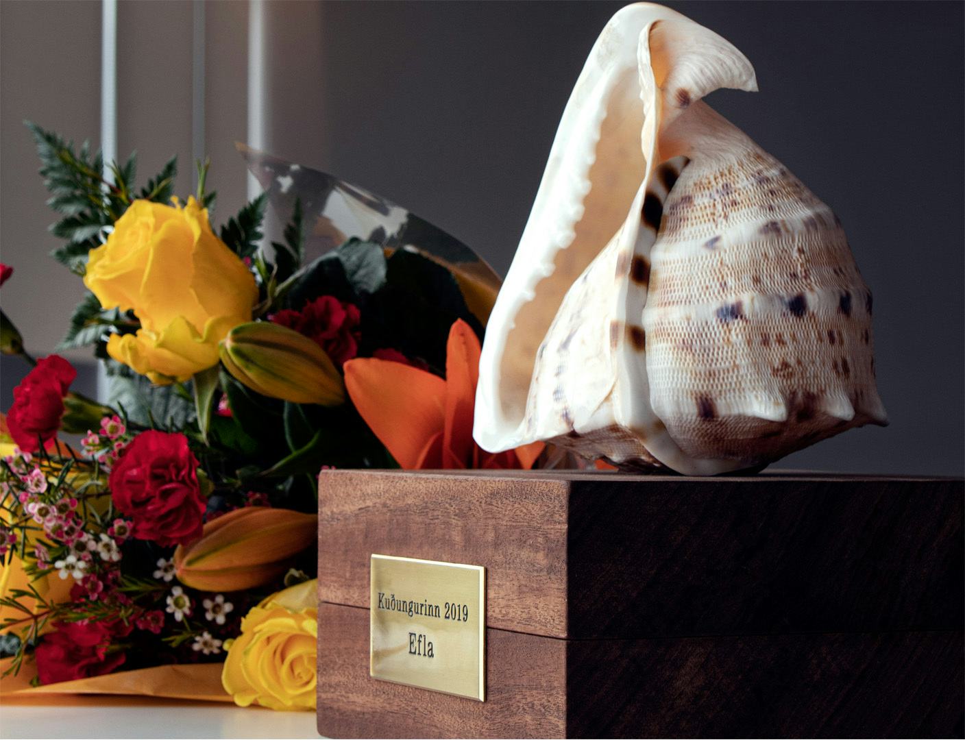 Sea shell on a wooden box, next to flower bouquet 