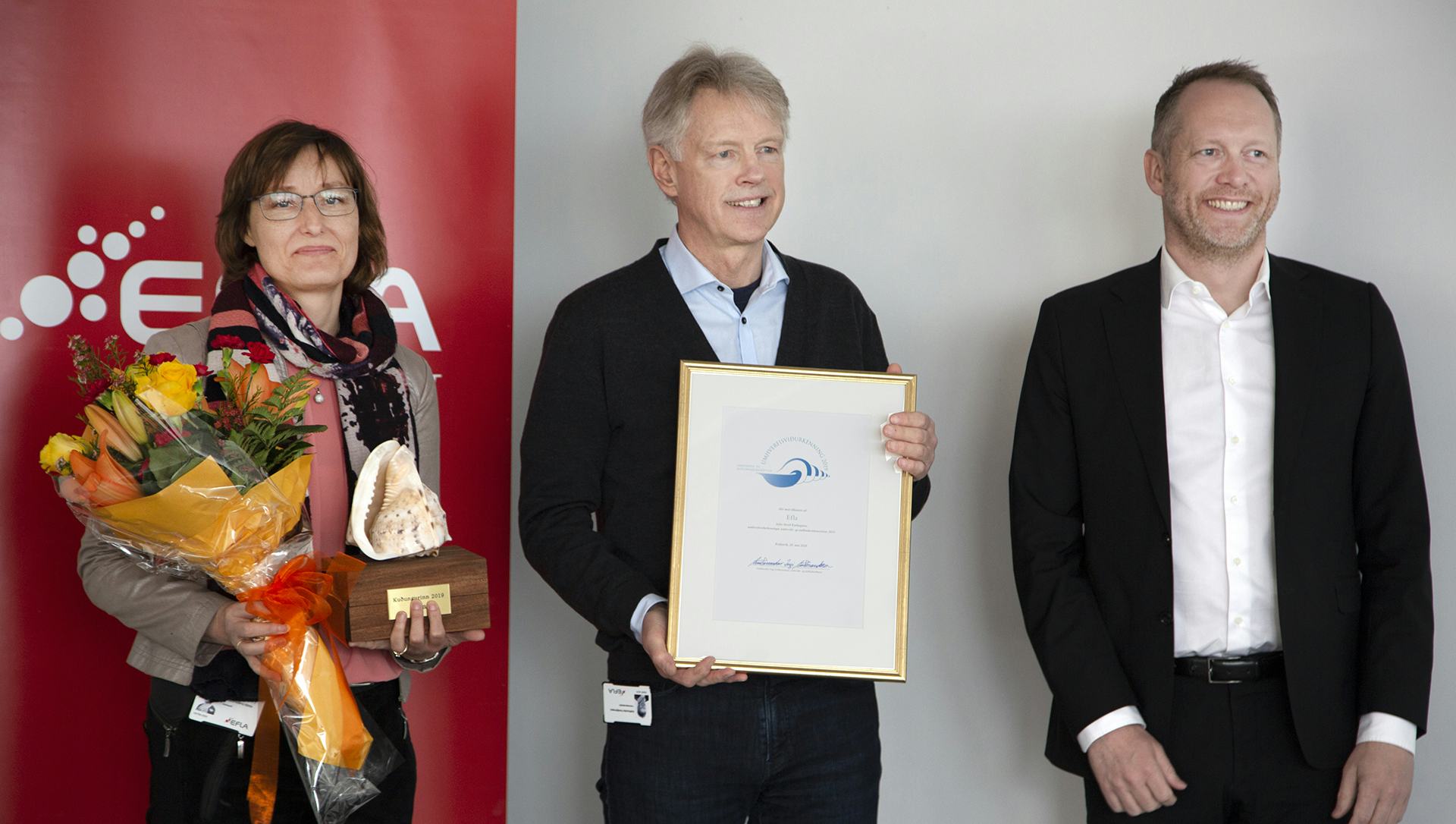 Three EFLA representatives holding Environmental award and flower bouquet 