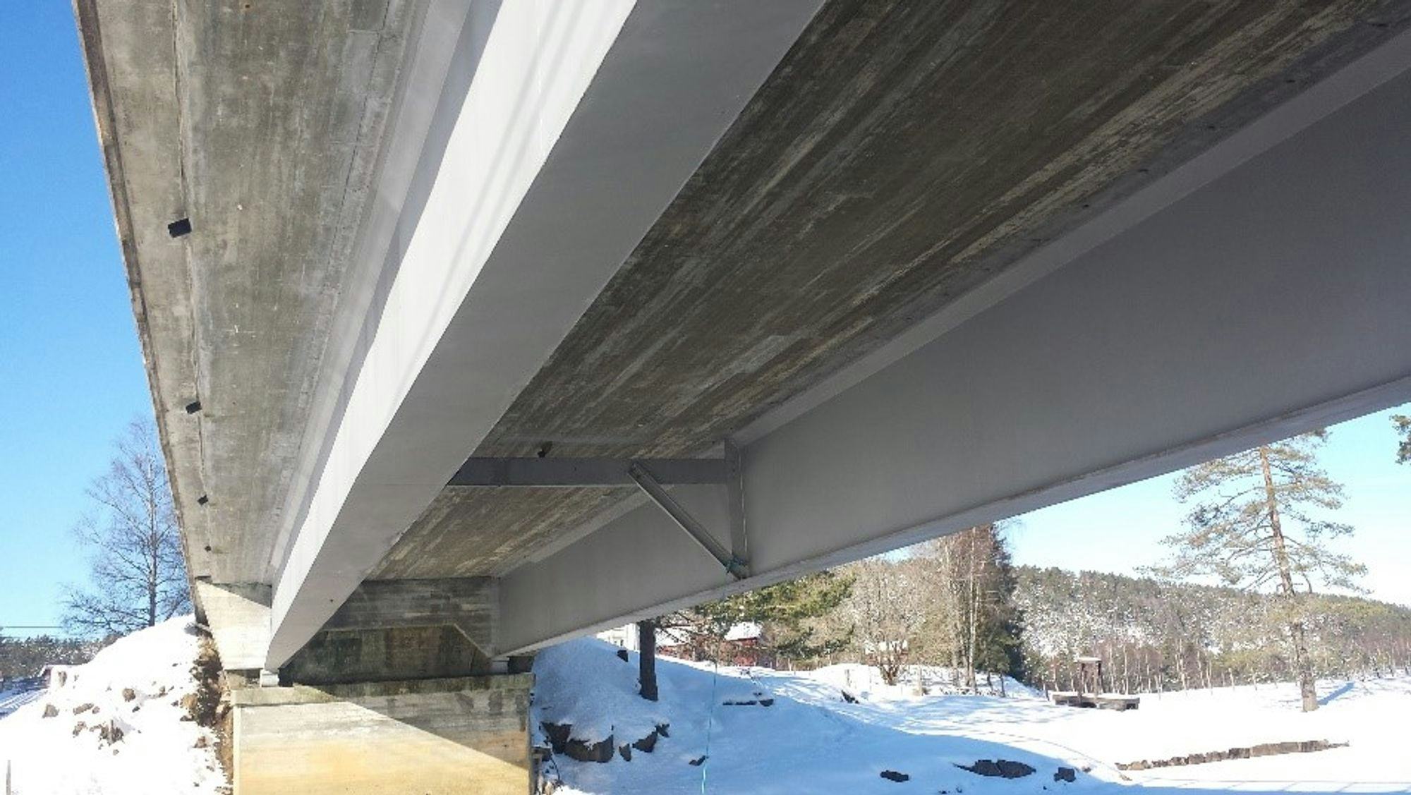 A view from underneath a traffic bridge, snow covered ground all around, woodland in the back 