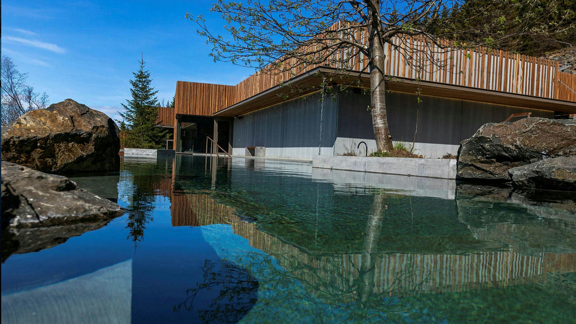 reflection of a wooden roof building on a pool and giant rocks placed around it