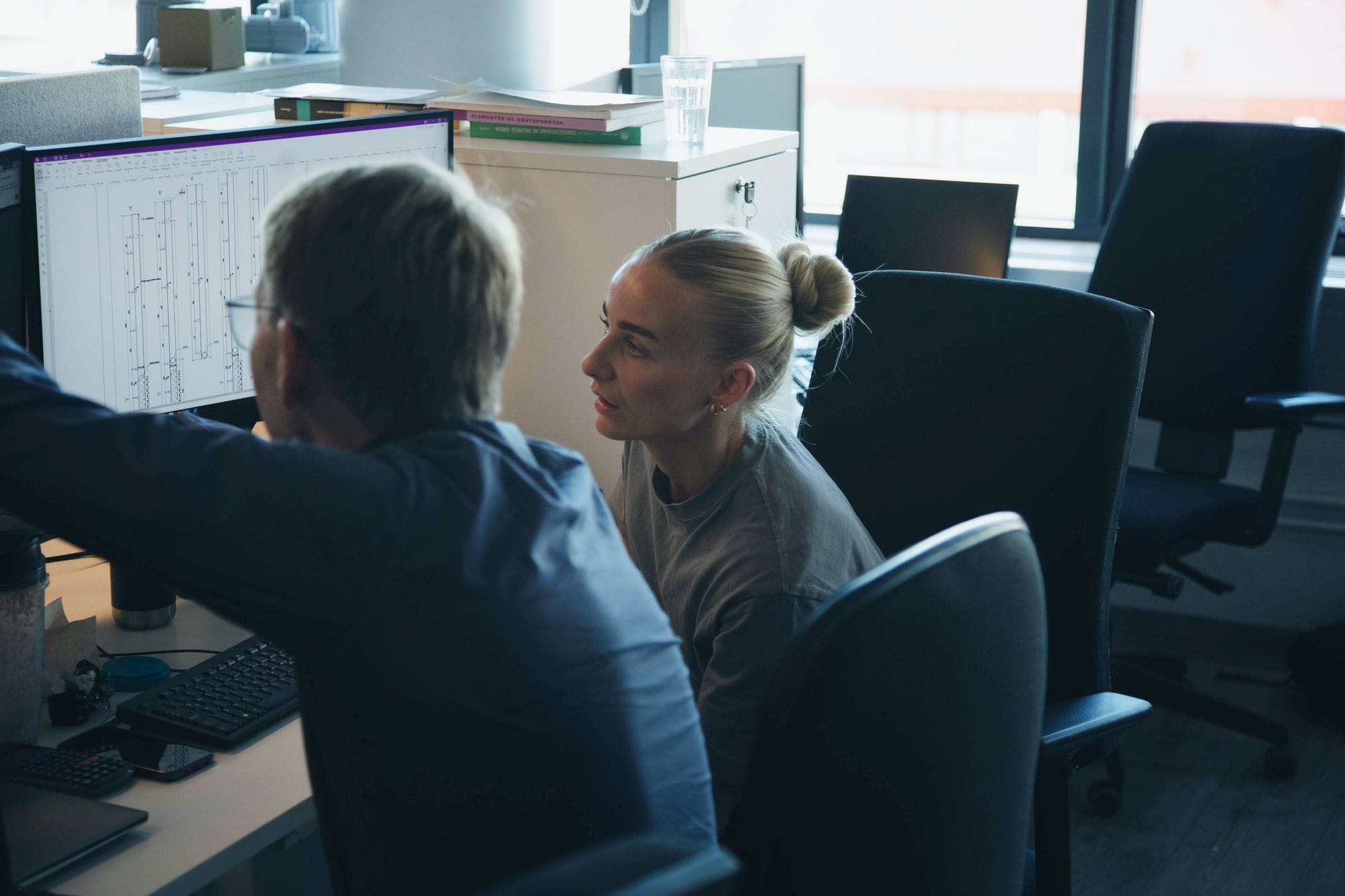 Man an a woman sitting at a computer screen in an office space, pointing at the screen and discussing