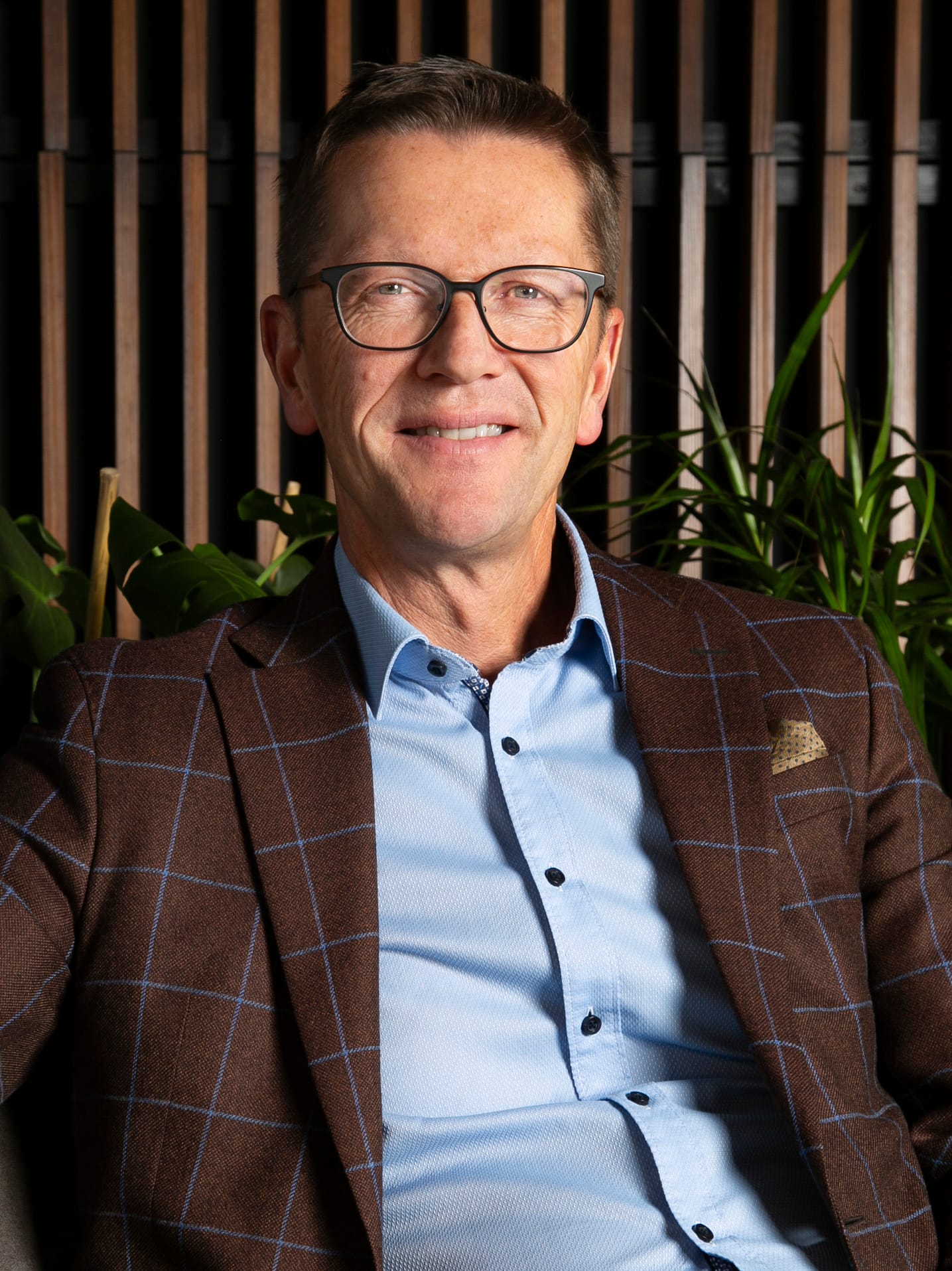 Portrait of a man, green plants and wooden panel in background